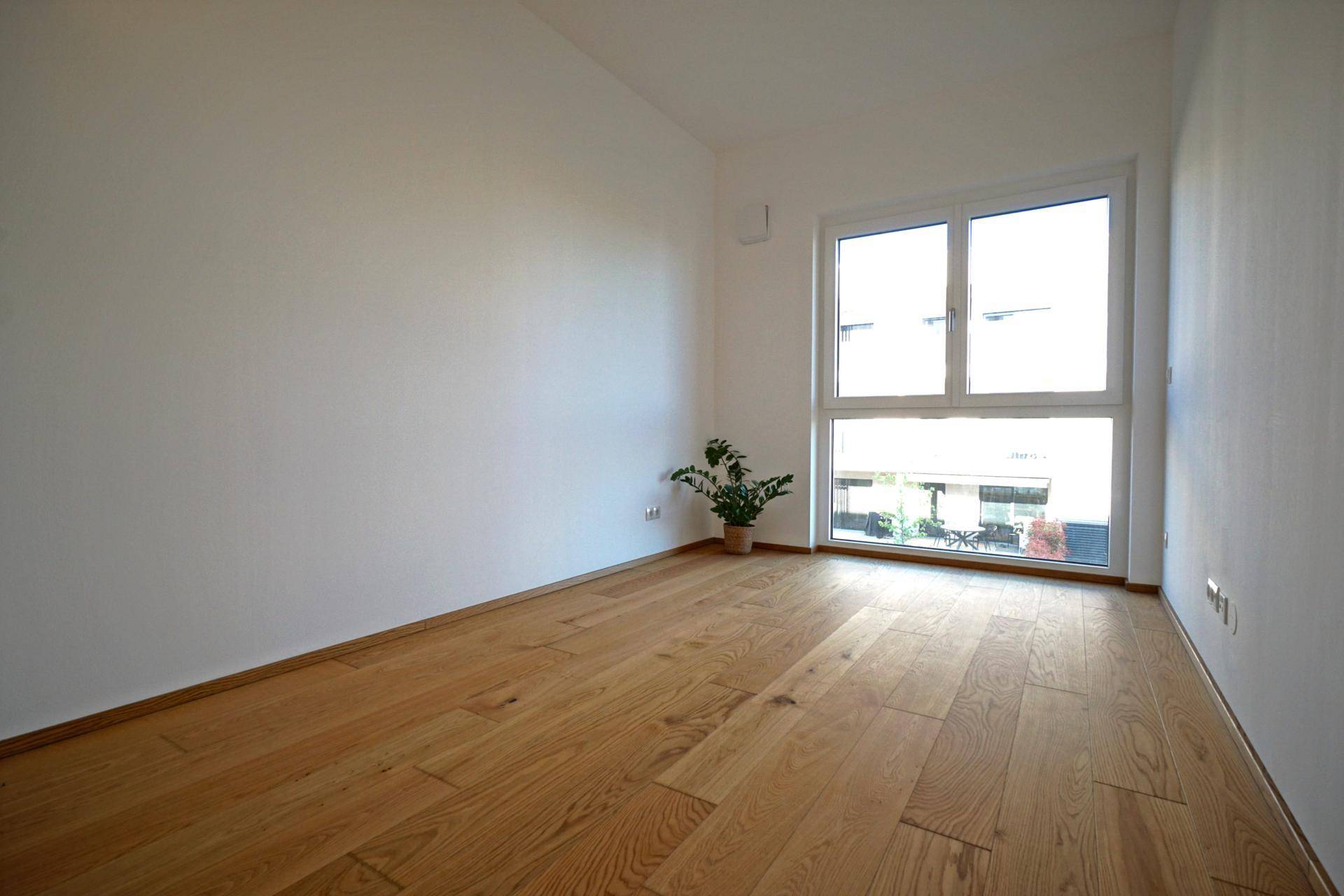 Helles Zimmer mit Holzboden und großem Fenster, ideal als Schlaf- oder Arbeitszimmer.
