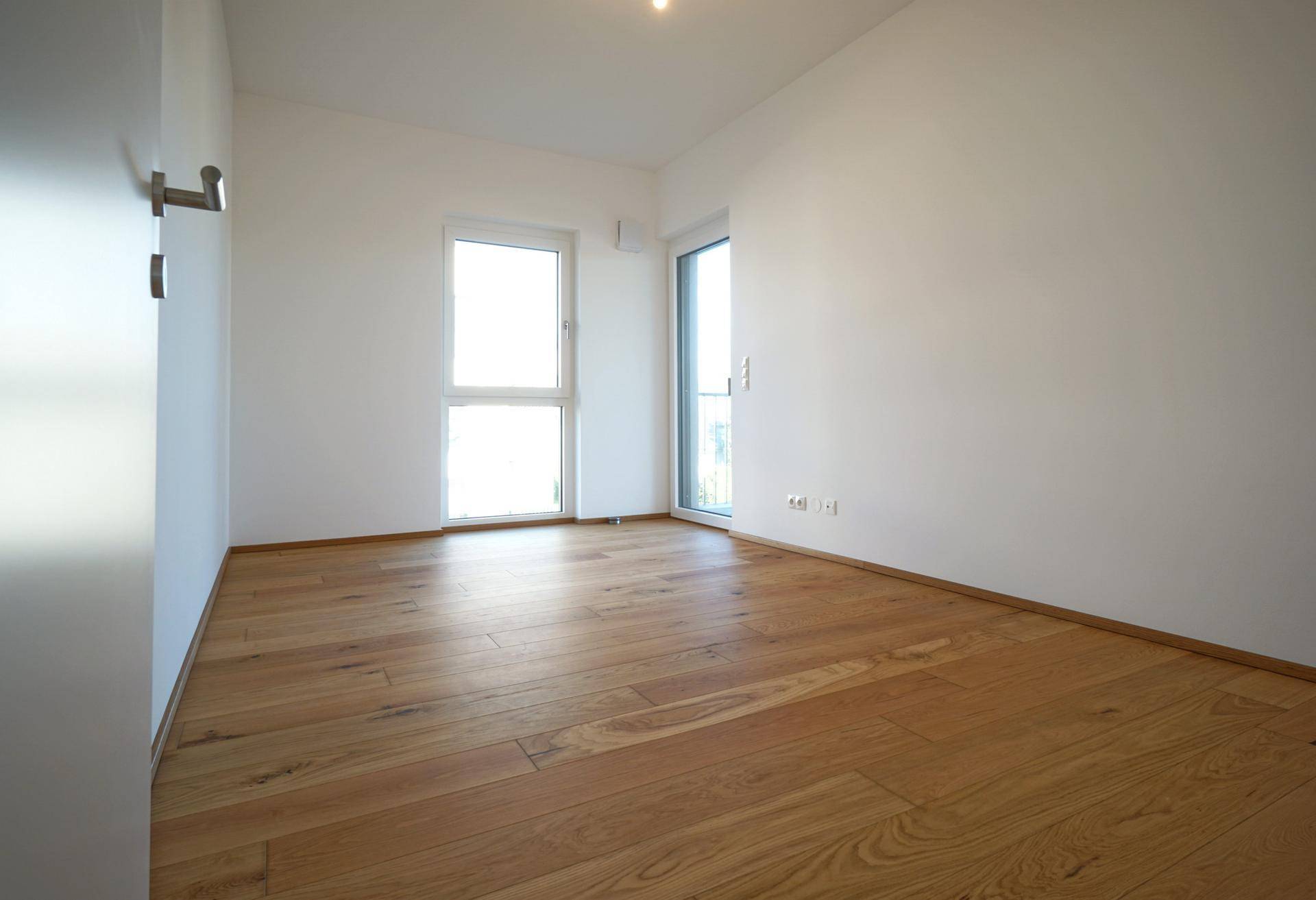 Helles Schlafzimmer mit Holzboden und Zugang zu einem französischen Balkon.