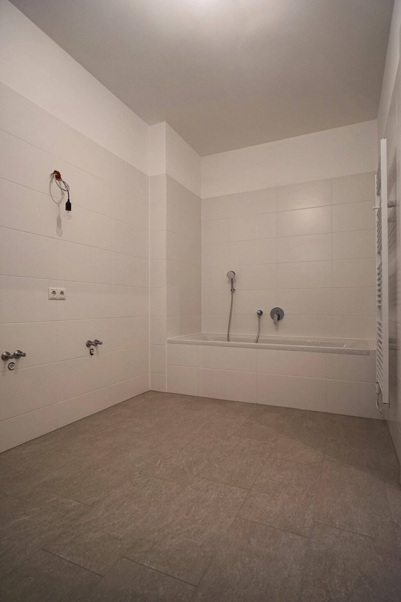 Geräumiges Badezimmer mit Badewanne, vorbereitet für eine Dusche, und Handtuchheizkörper.