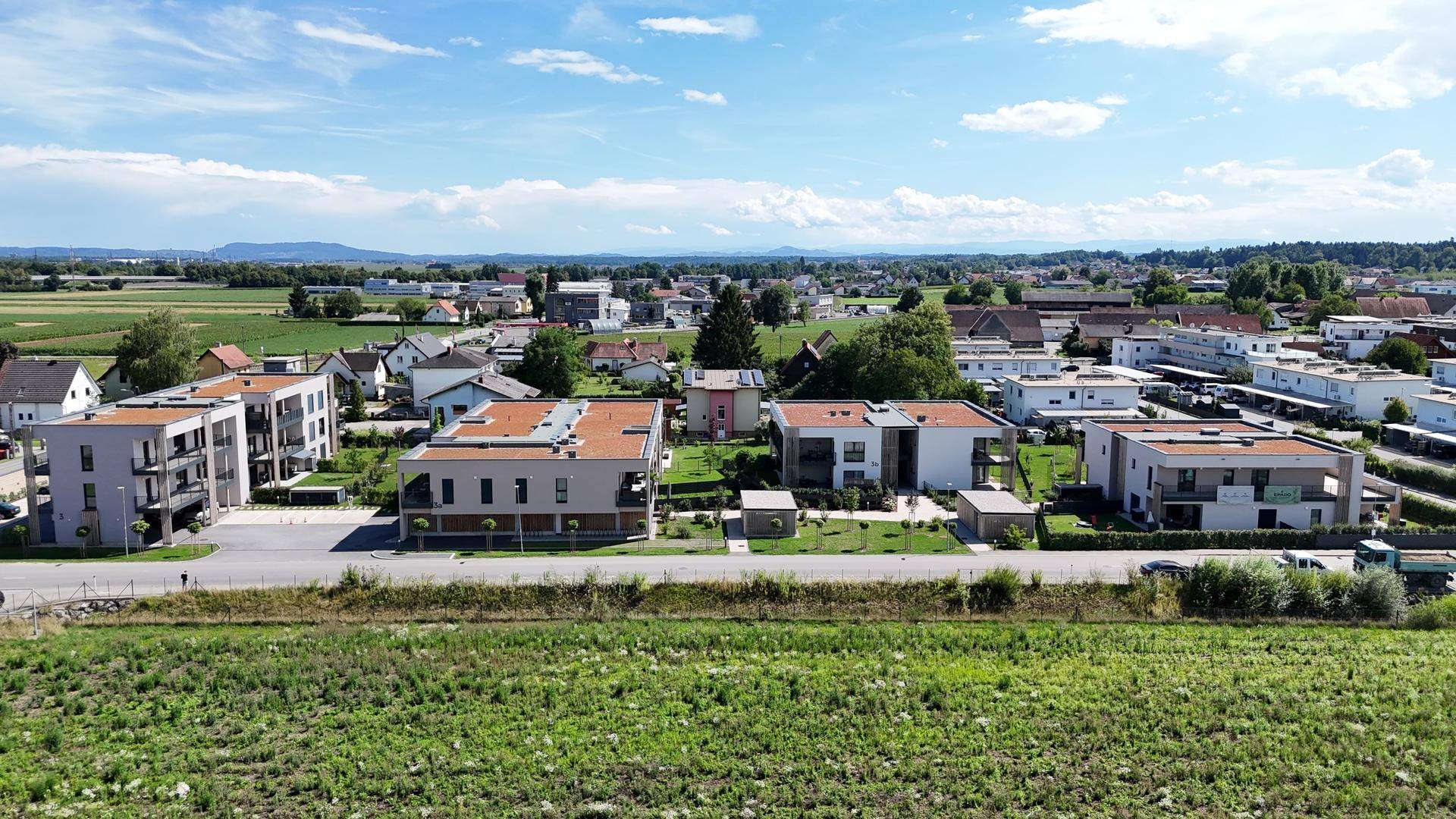 Weitläufige Ansicht der Wohnanlage mit umliegender Landschaft und Bergen im Hintergrund.