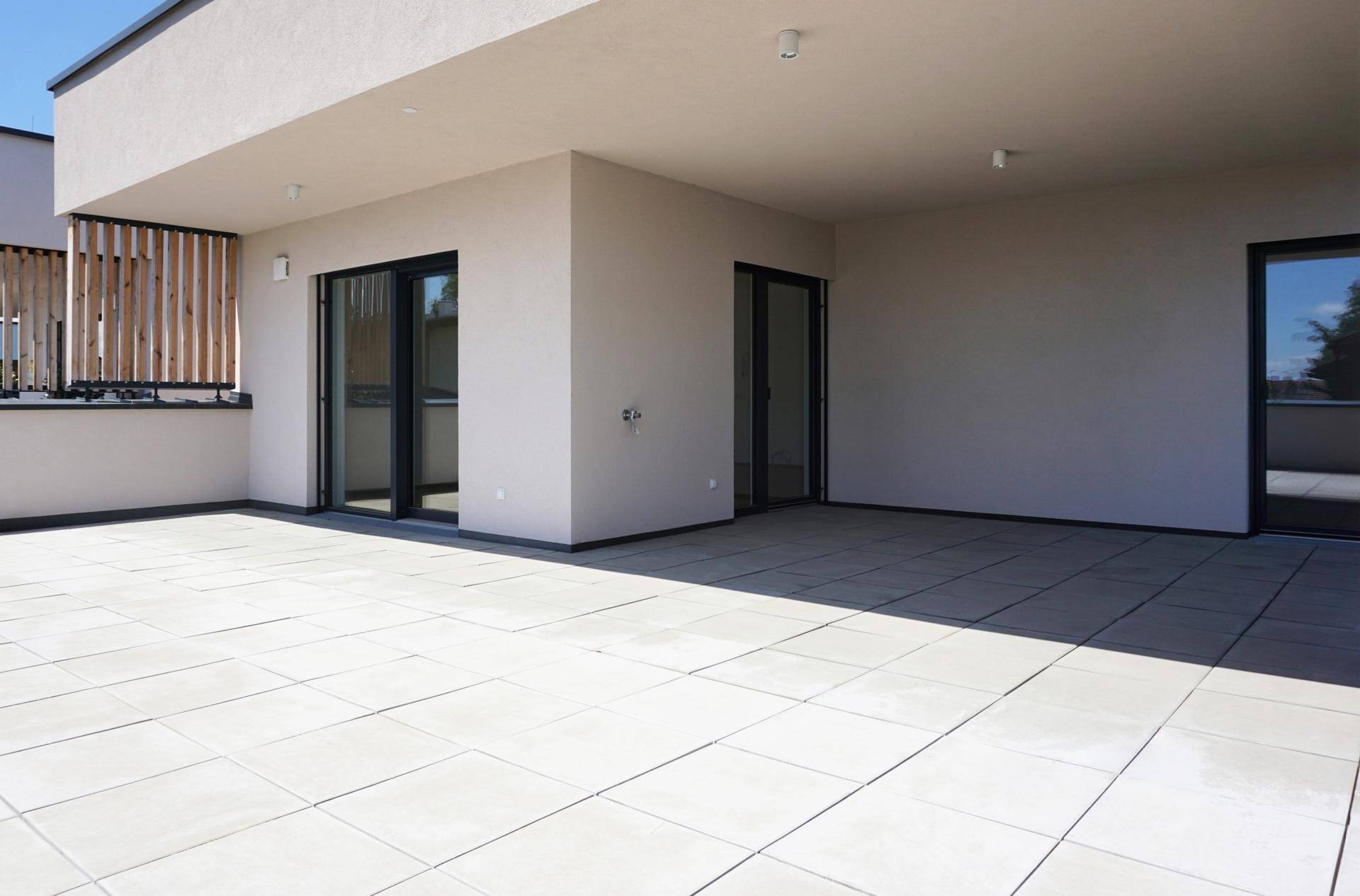 Weitläufige Terrasse mit Fliesenboden und modernen Schiebetüren zu den Innenräumen.