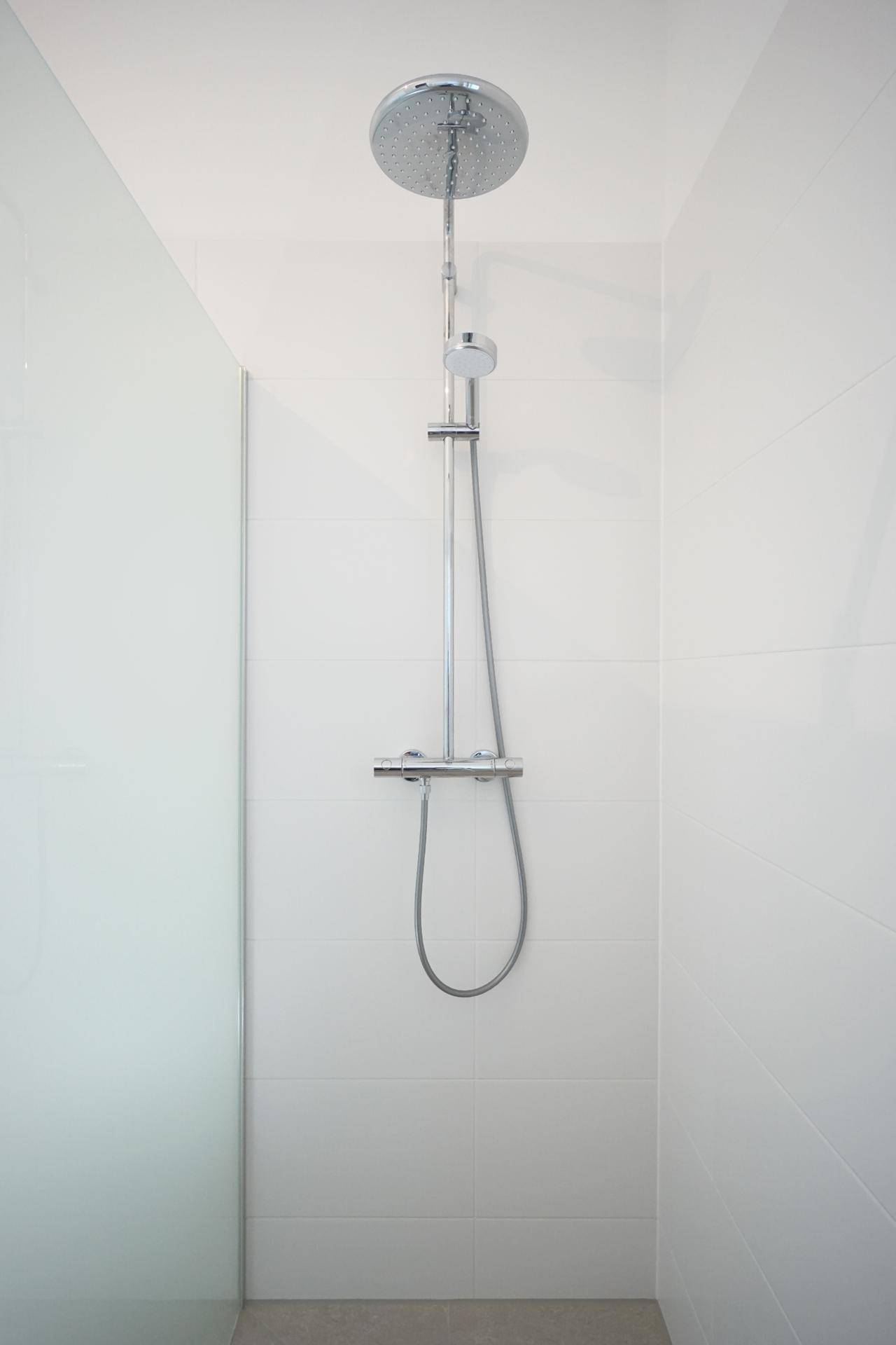 Moderne Dusche mit Regenduschkopf und minimalistischem Design in weiß gefliestem Bad.