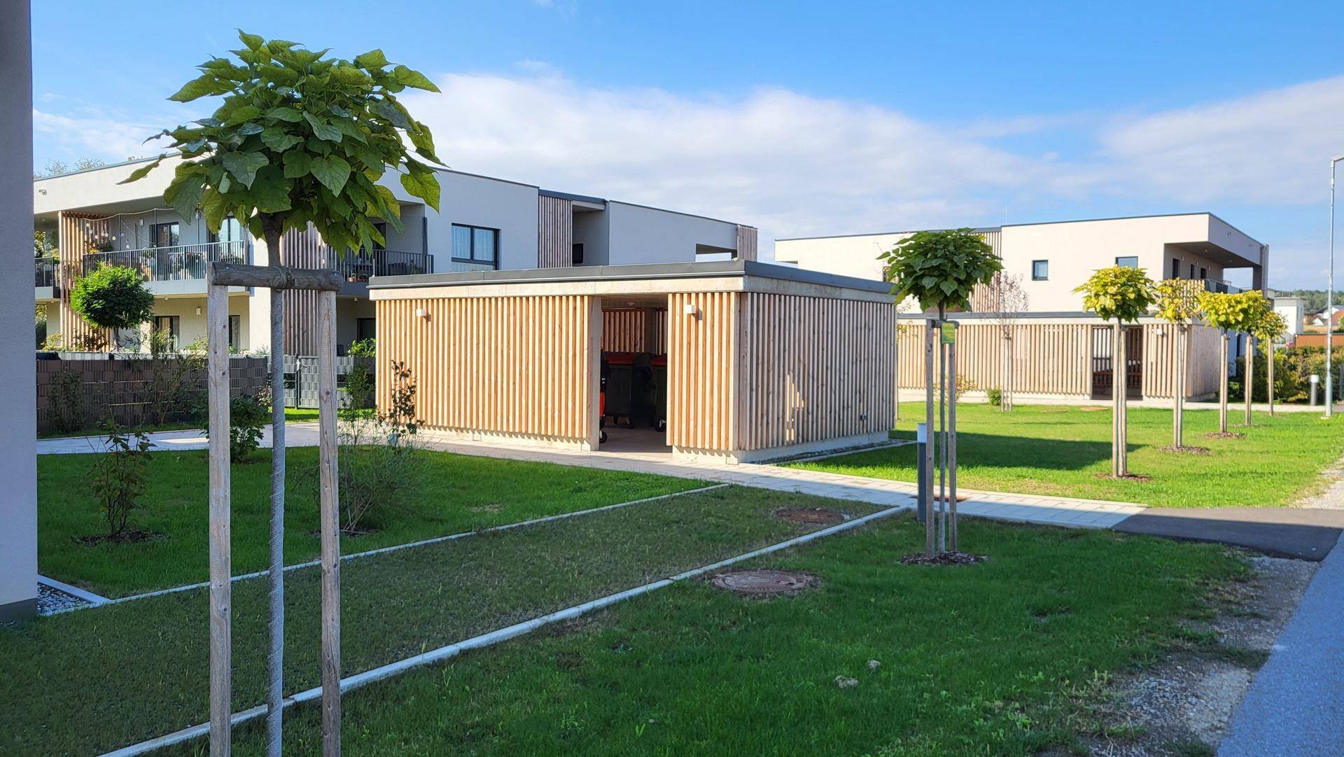 Gemeinschaftsbereich mit modernen Holzschuppen und gepflegten Rasenflächen.