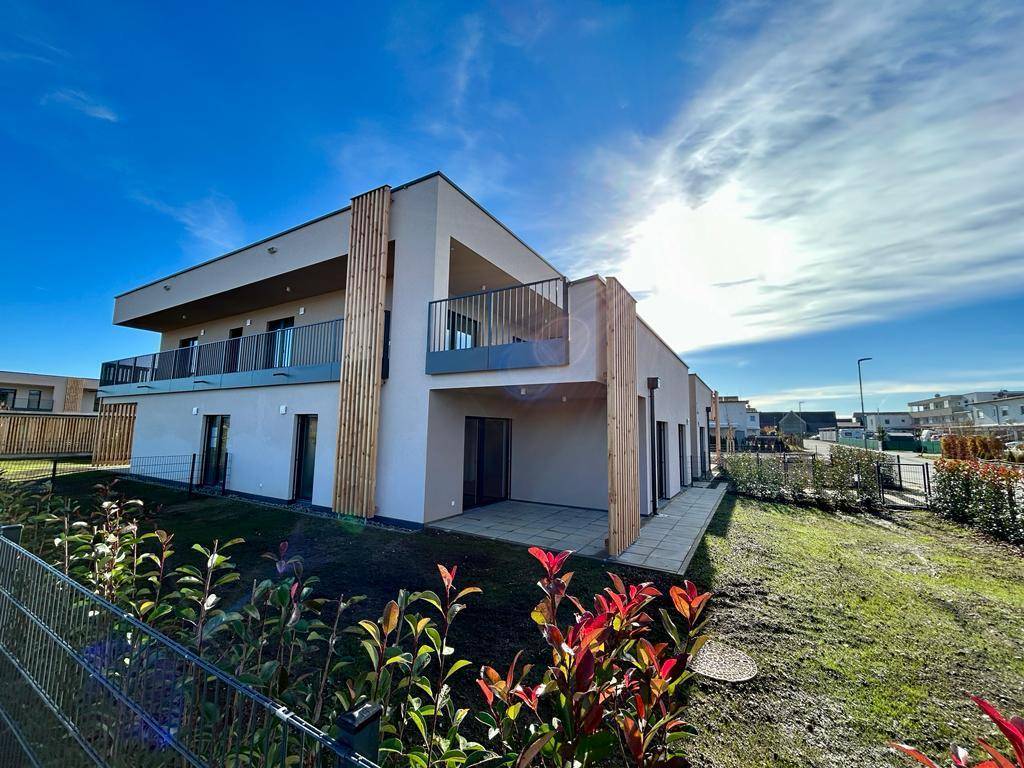 Seitenansicht eines modernen Gebäudes mit Terrasse und sonnigem Gartenbereich.