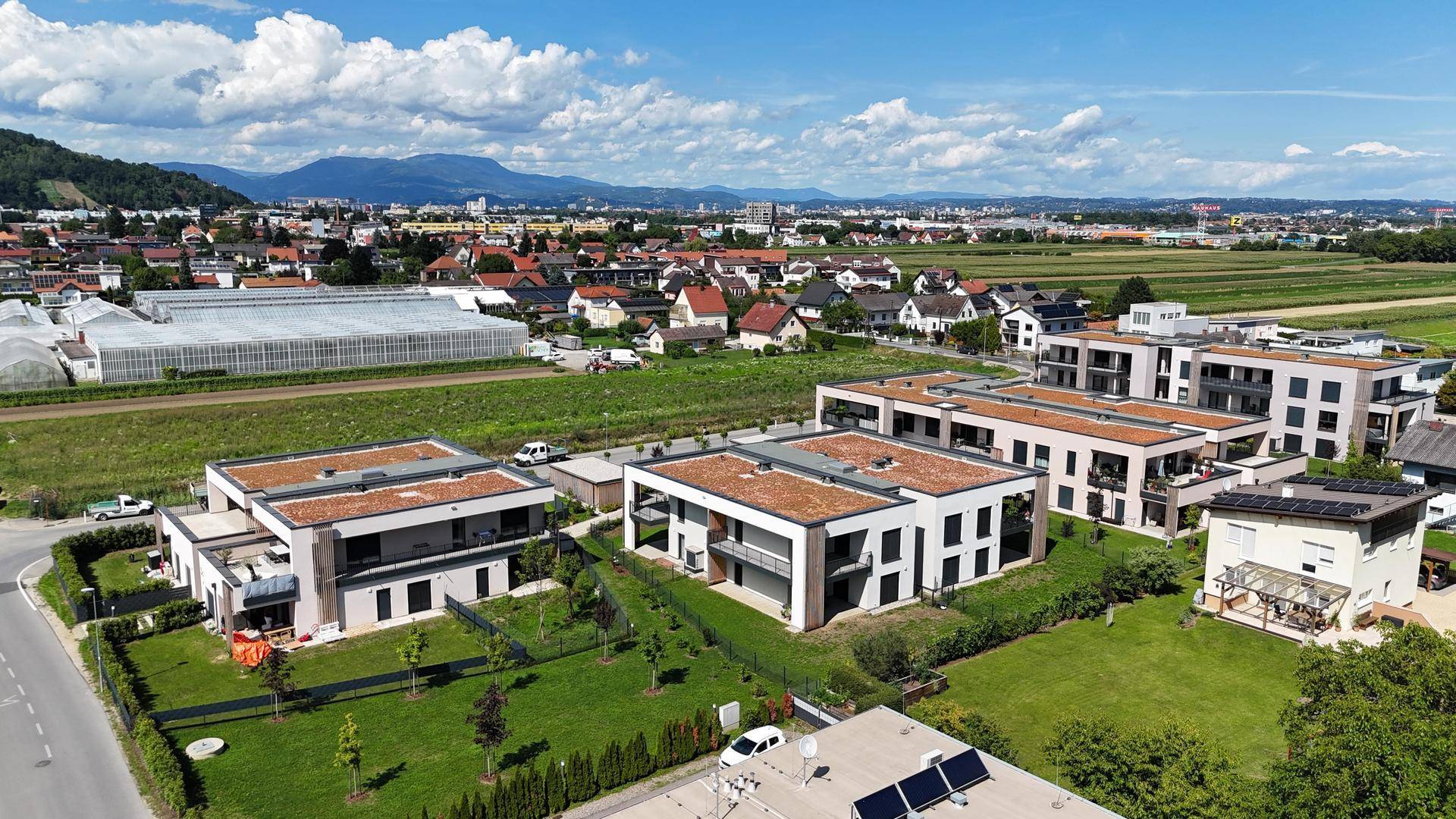 Weitläufige Ansicht der Wohnanlage mit umliegender Landschaft und Bergen im Hintergrund.
