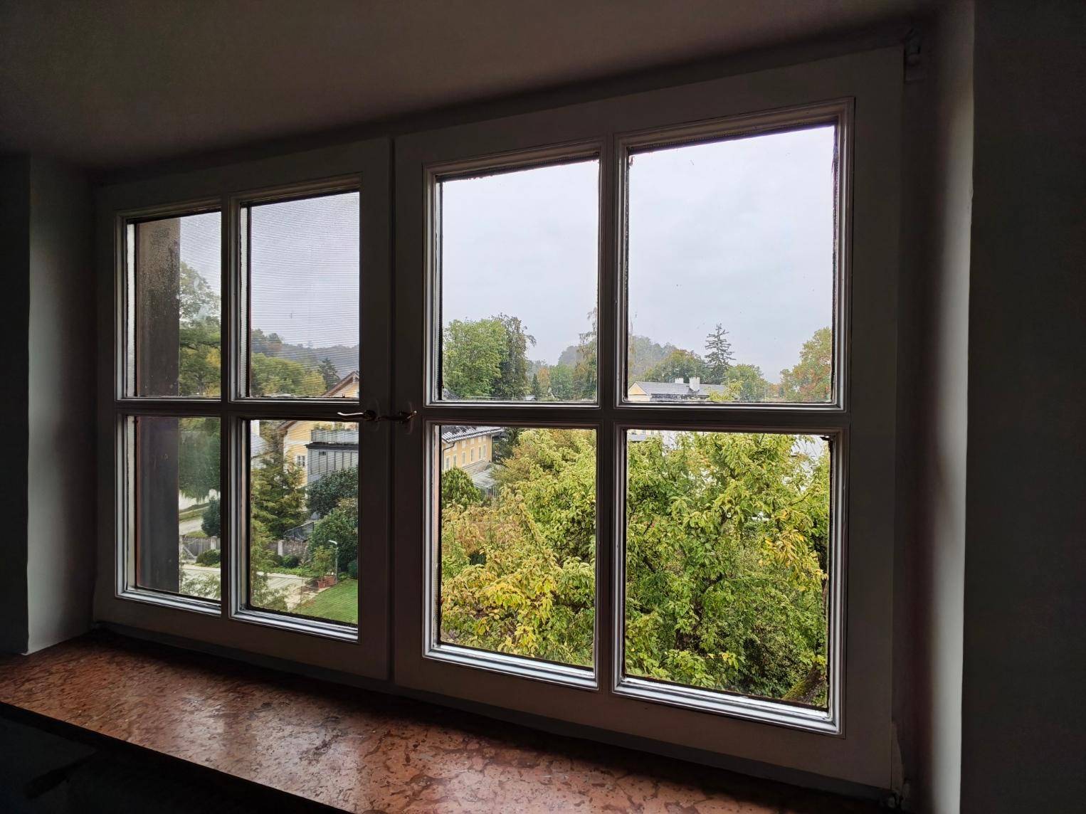 Fensterblick aus dem Schlafzimmer auf grüne Bäume und umliegende Häuser in ruhiger Lage.