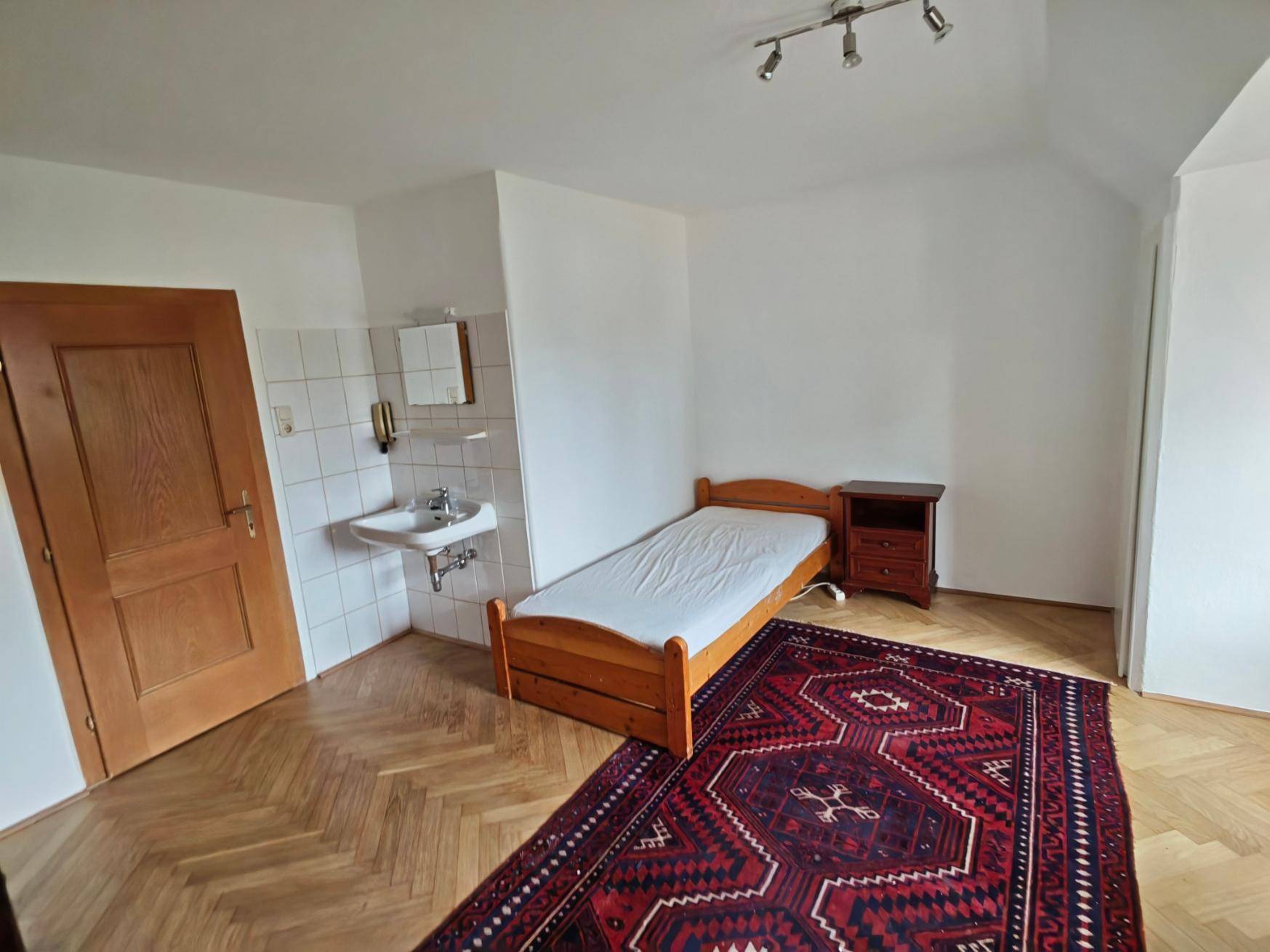 Gemütliches Schlafzimmer mit Holzparkett, Einzelbett und praktischem Waschbereich im Raum.