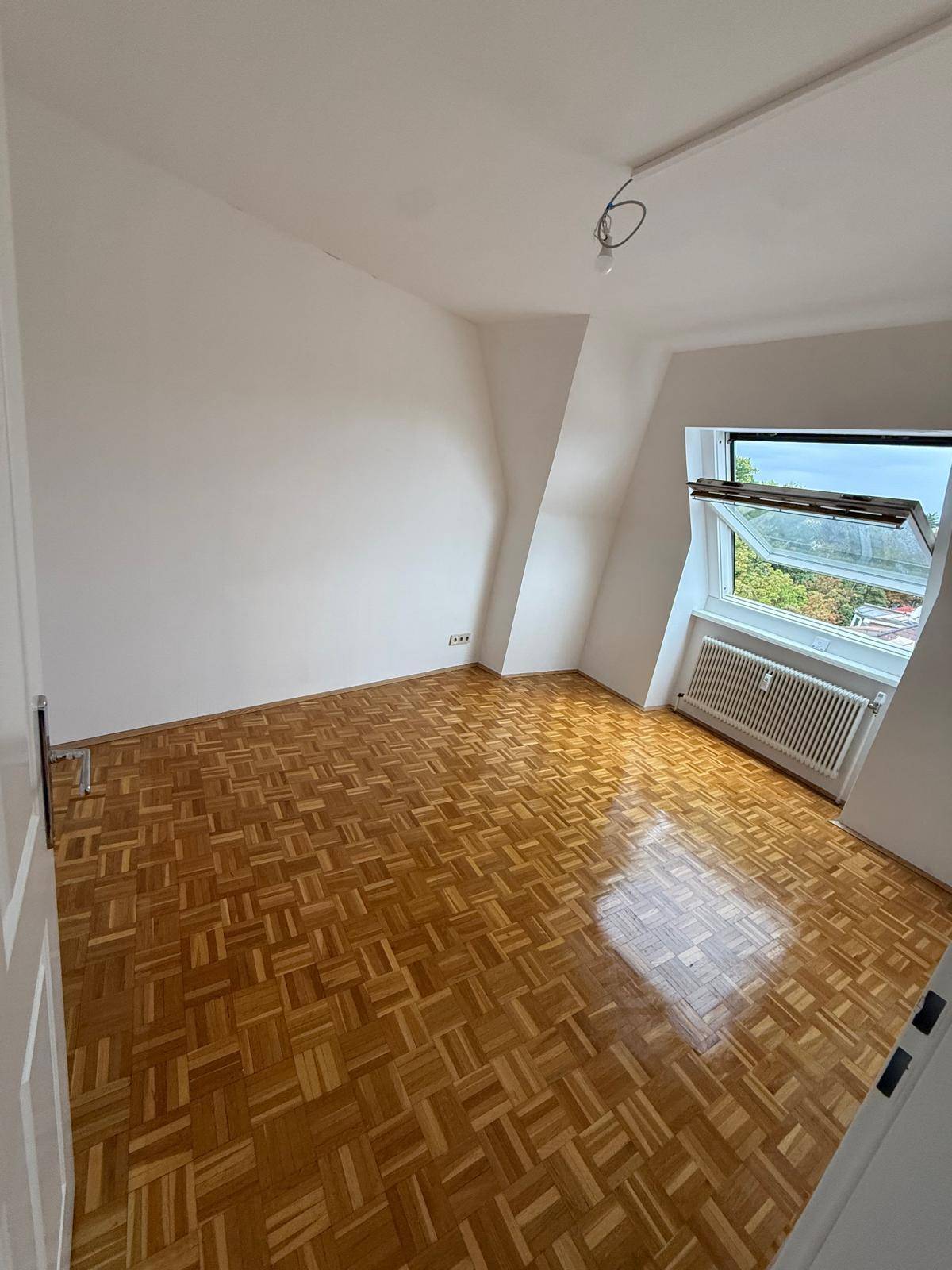Geräumiger Raum mit Parkettboden, weißen Wänden und einem großen Dachfenster, das viel Licht spendet.