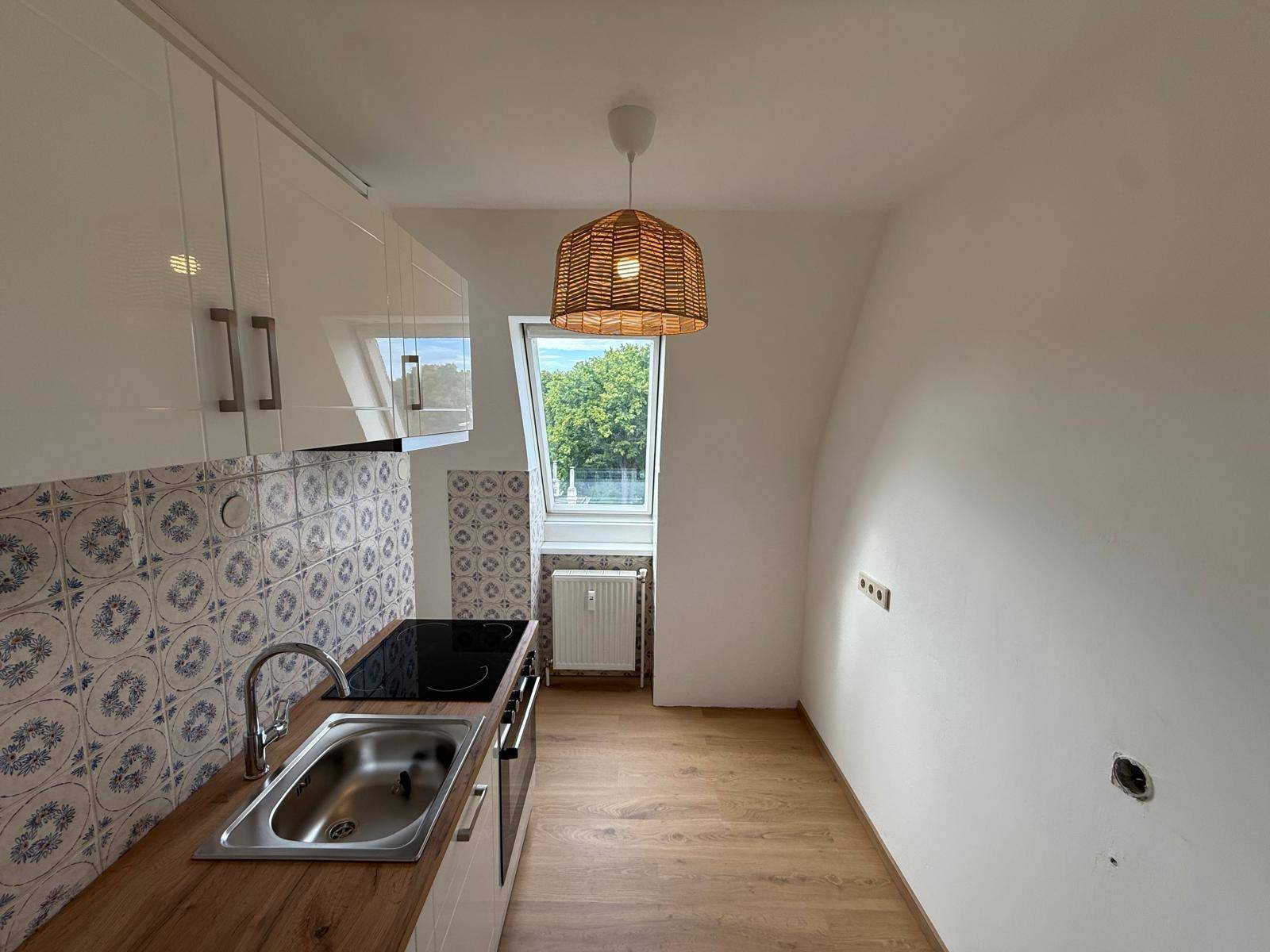 Moderne Küche mit weißen Hochglanzschränken, Holzarbeitsplatte, Induktionskochfeld und Dachfenster.