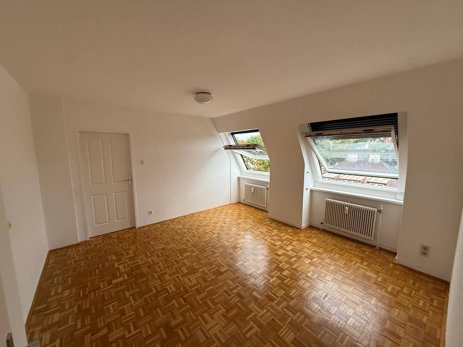 Heller Raum mit Parkettboden, weißen Wänden und zwei Dachfenstern, ideal für individuelle Gestaltung.