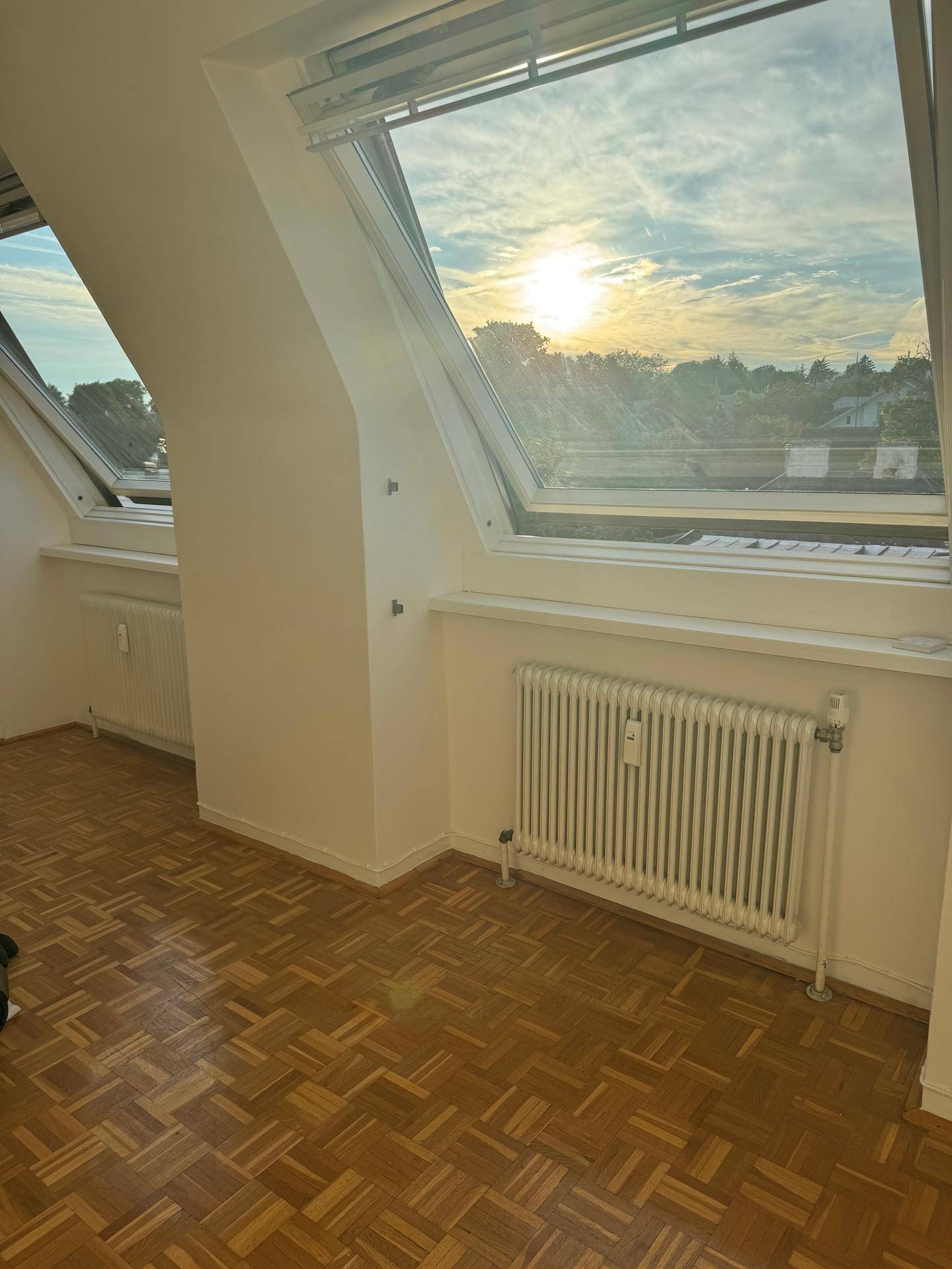 Heller Raum mit Parkettboden und zwei Dachfenstern, die einen schönen Blick auf den Sonnenuntergang bieten.