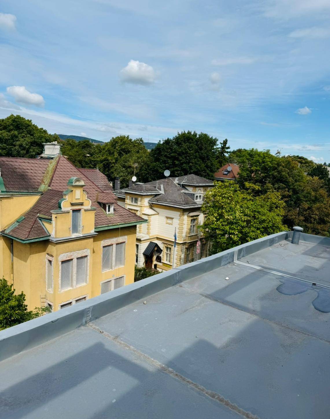 Blick von einem Flachdach auf charmante traditionelle Gebäude mit Satteldächern und viel Grün.