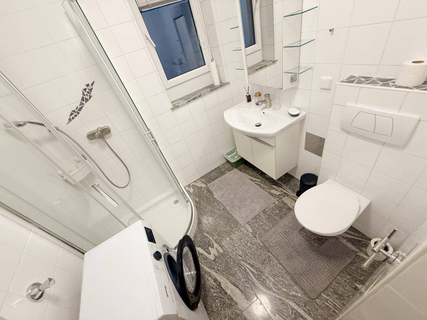 Modernes Badezimmer mit Duschkabine, WC, Waschbecken und einem Fenster für natürliche Belüftung.