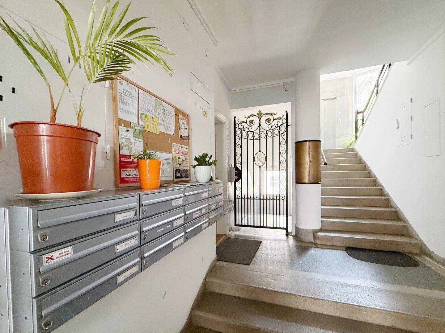 Eingangsbereich eines Mehrfamilienhauses mit Briefkästen, Treppenhaus und dekorativem Metalltor.