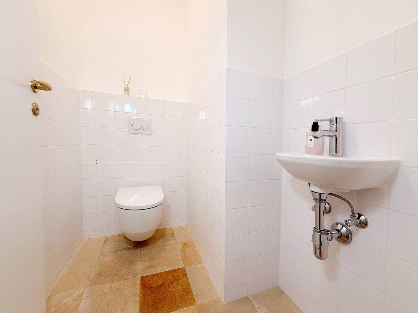 Kleines Gäste-WC mit weißen Fliesen, wandhängender Toilette und einem kompakten Waschbecken.