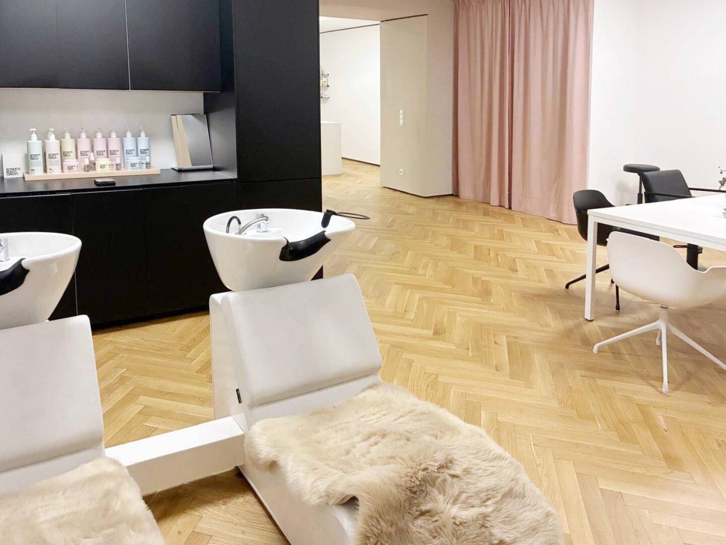 Moderner Friseursalon mit Waschsesseln, dunklen Schränken und hellem Fischgrätparkett.