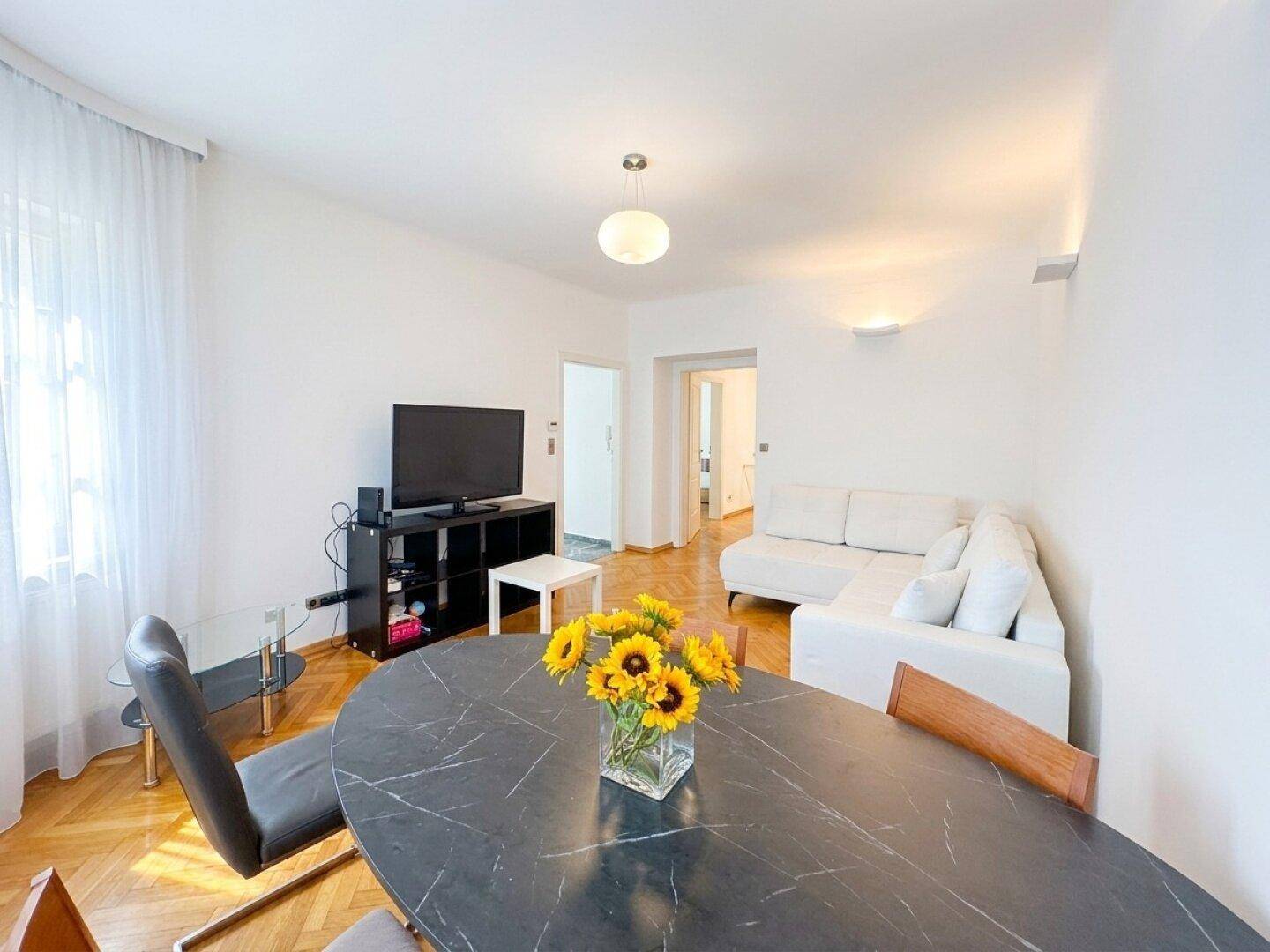 Gemütlicher Wohn- und Essbereich mit modernem Esstisch, bequemer Couch und Zugang zu weiteren Räumen.