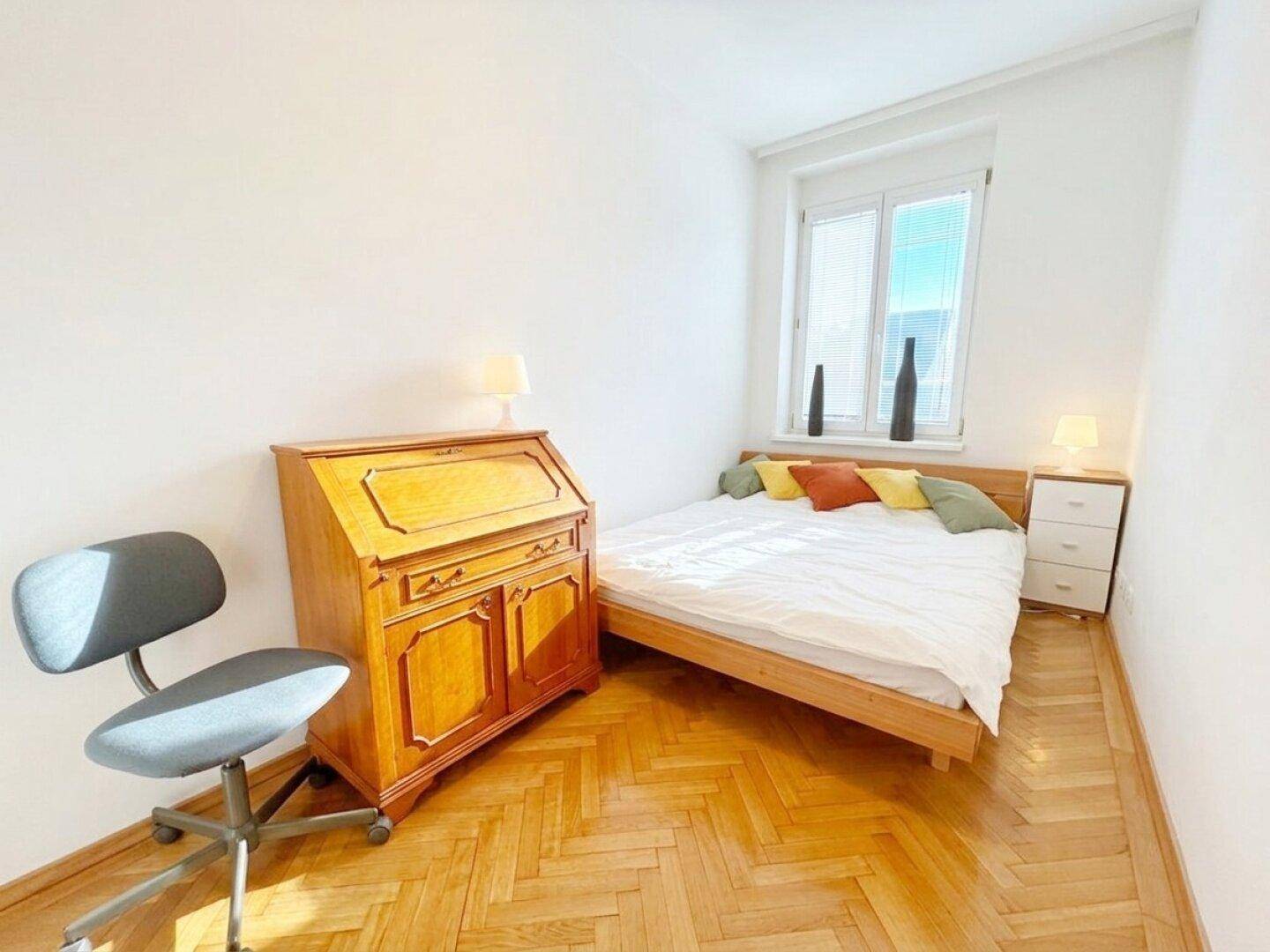Gemütliches Schlafzimmer mit Holzbett, antikem Sekretär und viel Tageslicht durch das Fenster.