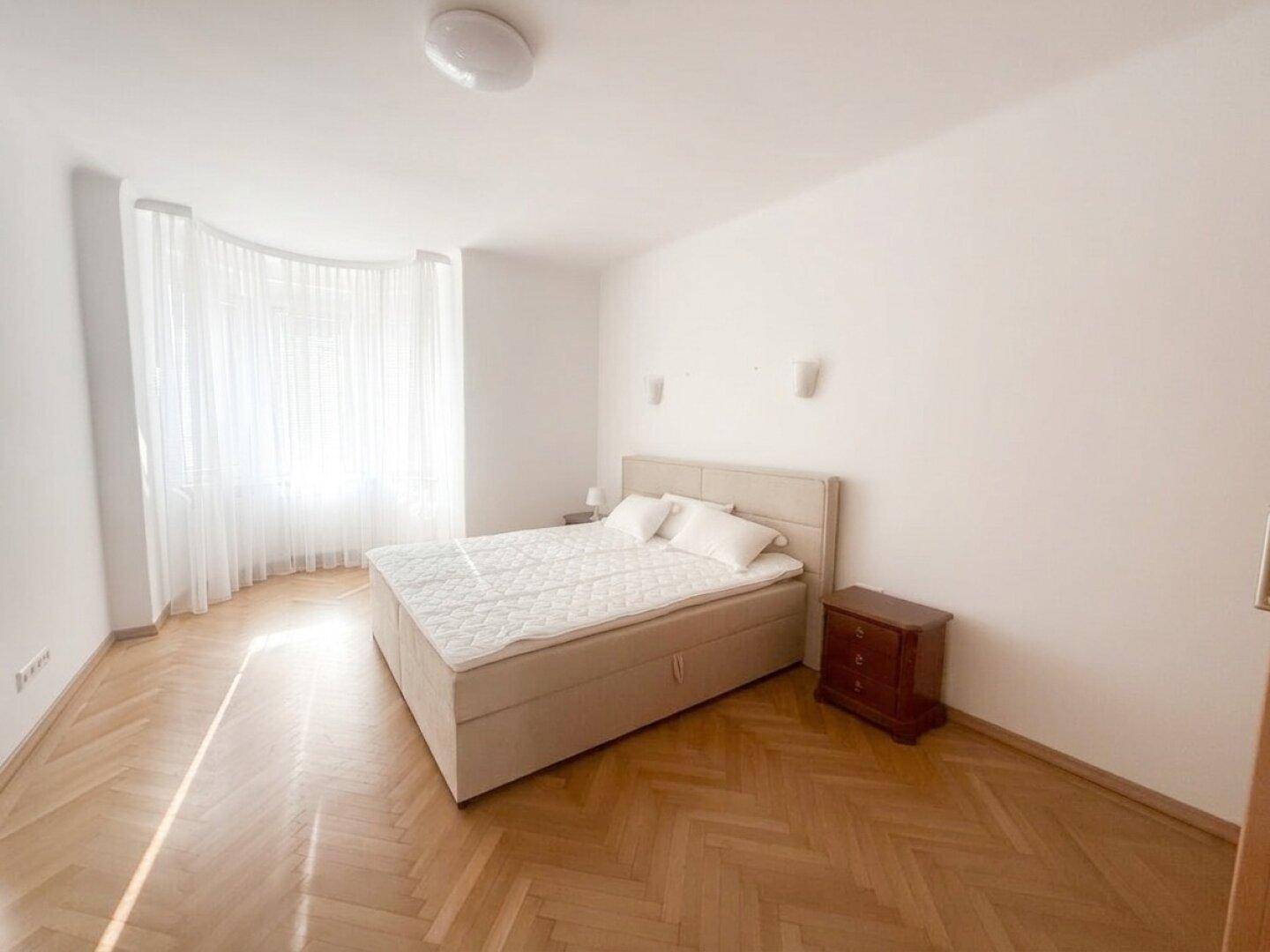 Lichtdurchflutetes Schlafzimmer mit großem Fenster, Fischgrätparkett und einem bequemen Doppelbett.