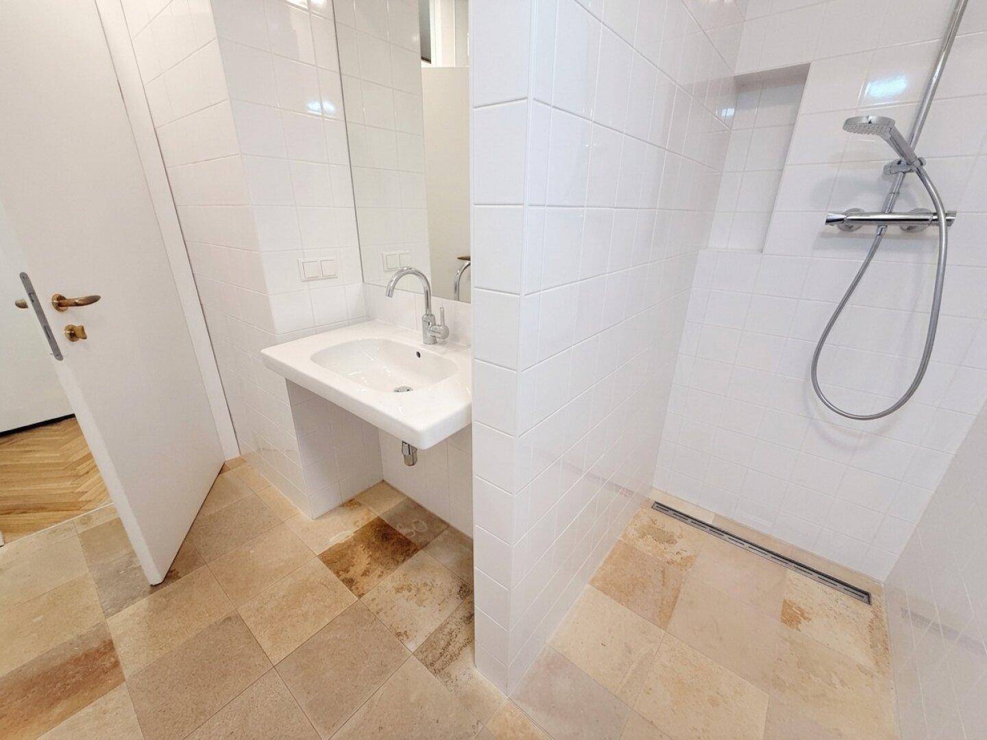 Modernes Badezimmer mit weißen Fliesen, wandhängendem Waschbecken und einer begehbaren Dusche.