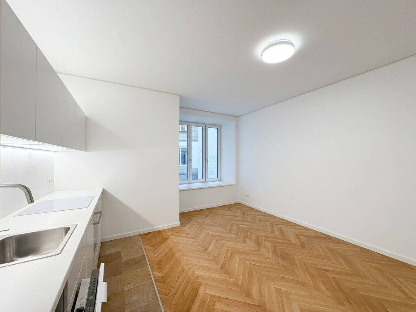 Moderne weiße Küchenzeile mit integrierten Geräten, Fischgrätparkett und einem Fenster.