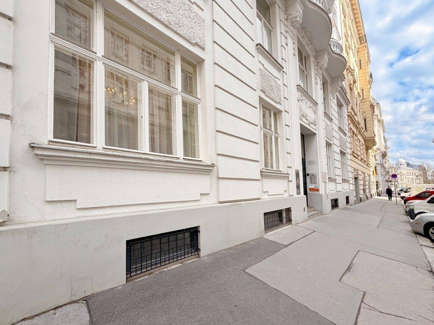 Seitenansicht einer Gebäudefassade mit Fenstern und einem Bürgersteig in der Stadt.
