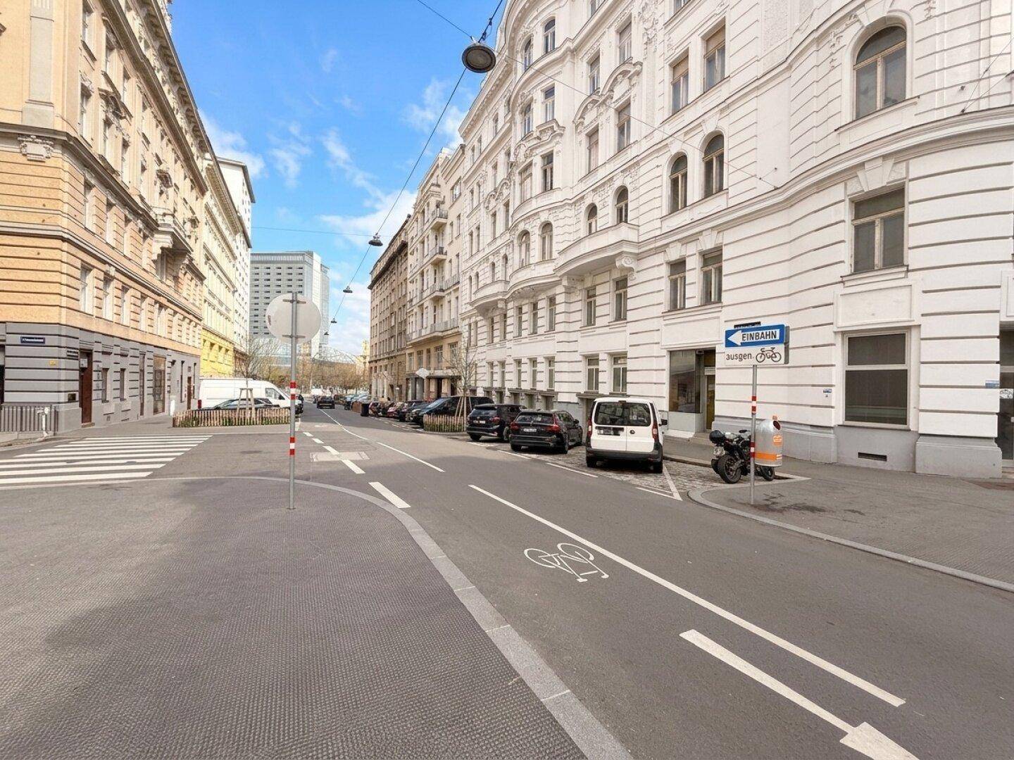 Stadtstraße mit historischen Gebäuden, parkenden Autos und einem klaren blauen Himmel.