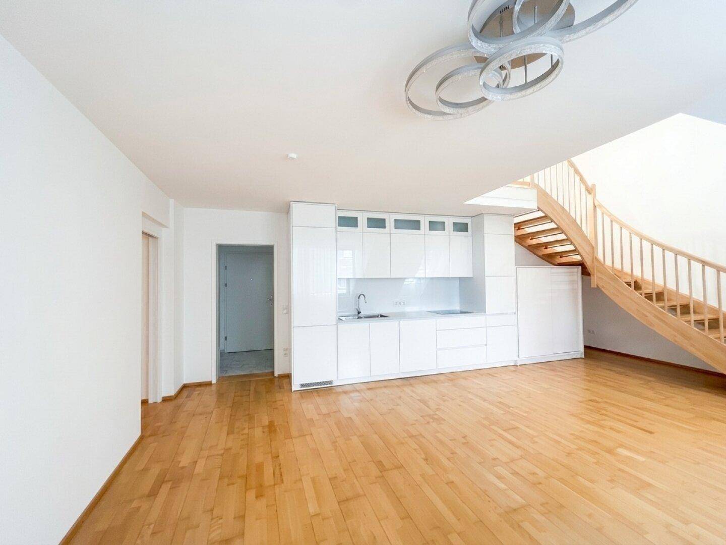 Geräumiger Wohnbereich mit integrierter Küchenzeile und eleganter Holztreppe zum Obergeschoss.