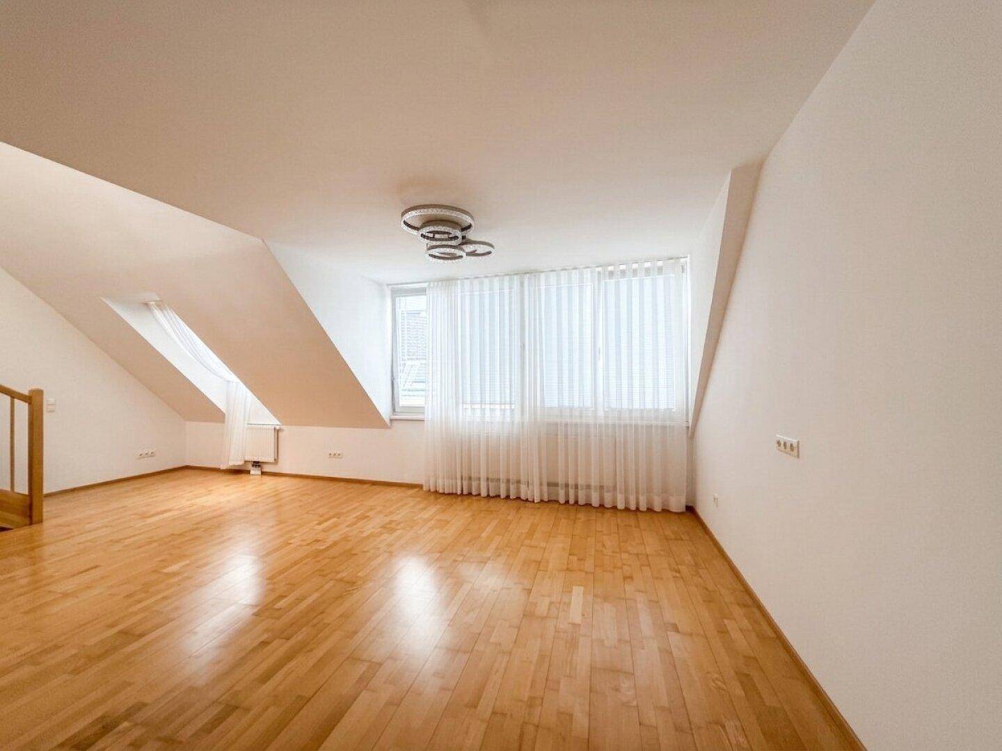 Geräumiger Wohnraum im Dachgeschoss mit Holzboden, großen Fenstern und Dachschrägen.