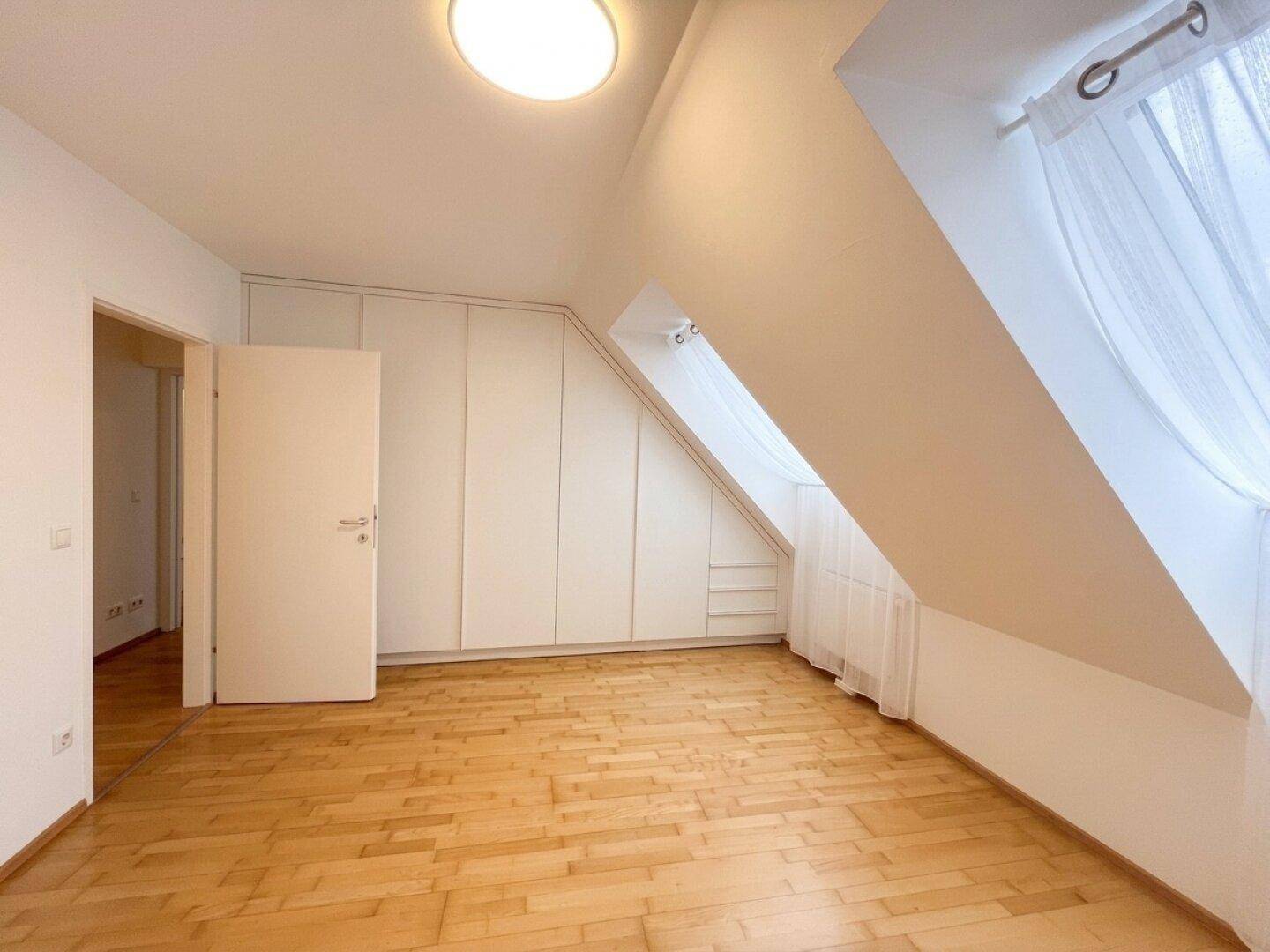 Helles Schlafzimmer im Dachgeschoss mit maßgefertigten Einbauschränken und Holzboden.