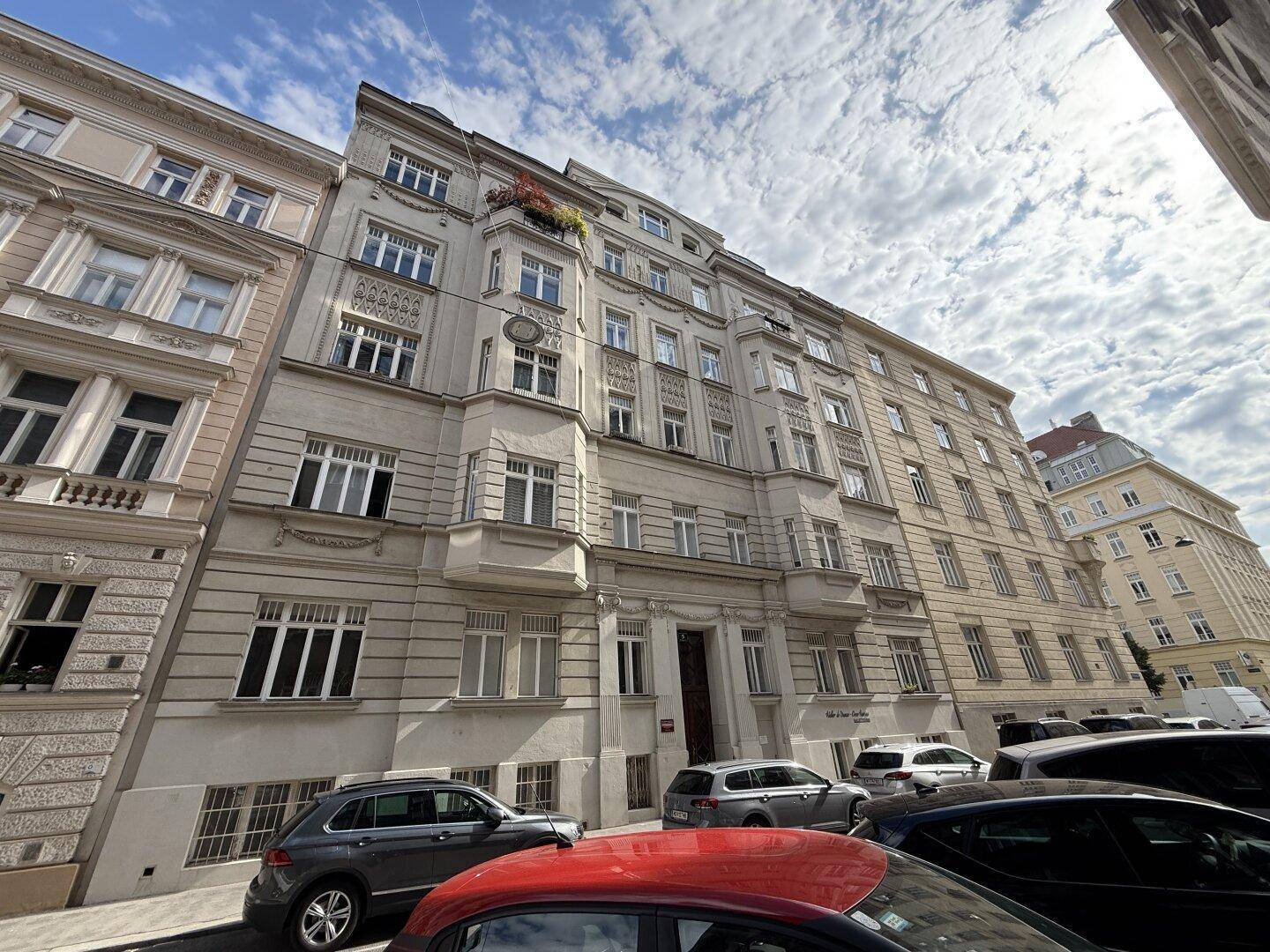Mehrstöckiges Altbaugebäude mit vielen Fenstern und geparkten Autos auf der Straße.