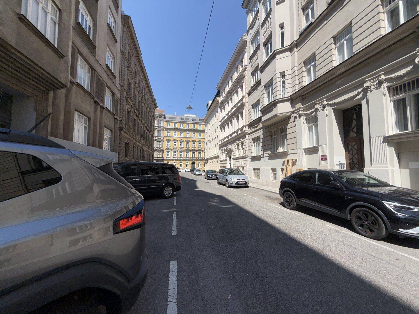 Eine belebte Straße mit geparkten Autos und historischen Gebäuden unter blauem Himmel.