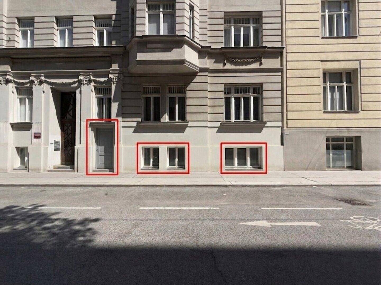 Fassade eines Gebäudes an einer Straße, mit rot markierten Eingängen und Fenstern im Erdgeschoss.