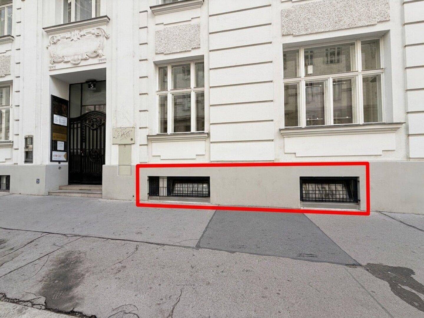 Fassade eines weißen Altbaus mit repräsentativem Eingangsbereich und vergitterten Kellerfenstern zur Straße hin.