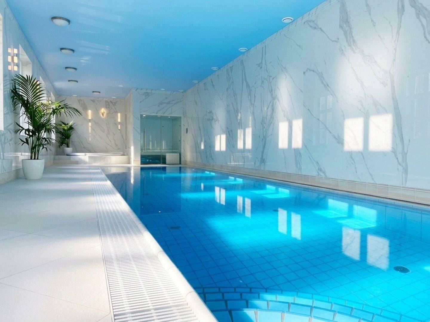 Luxuriöser Innenpoolbereich mit Marmorwänden, blauen Fliesen und viel Tageslicht.