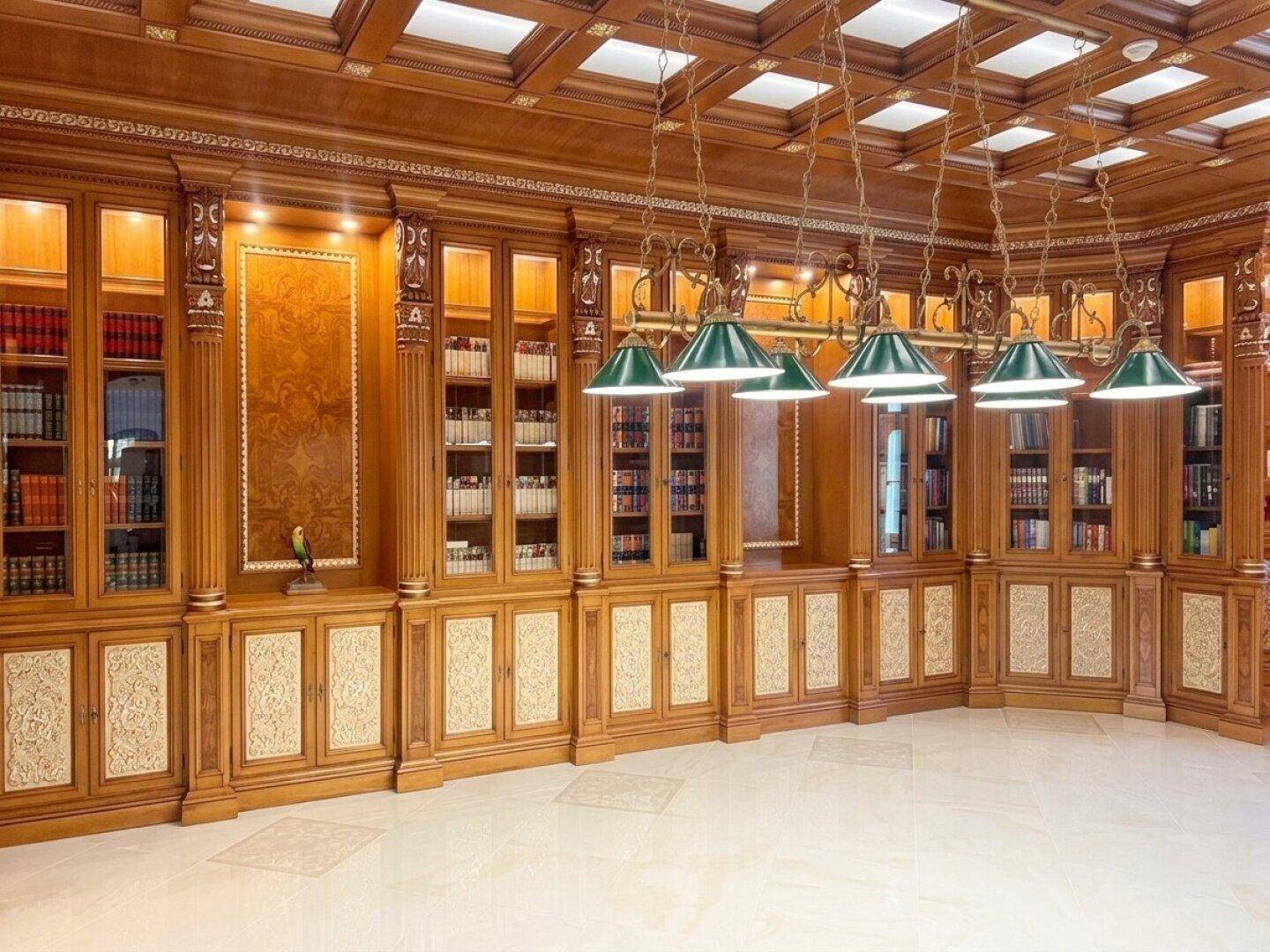 Exklusive Bibliothek mit raumhohen Holzregalen, aufwendiger Deckenverkleidung und Leselampen.