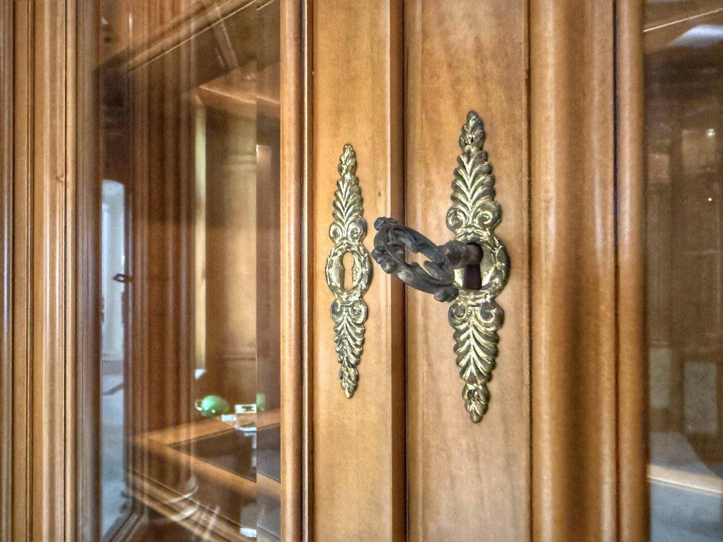 Detailaufnahme eines antiken Holzschranks mit kunstvollem Messingschlüssel und Beschlägen.