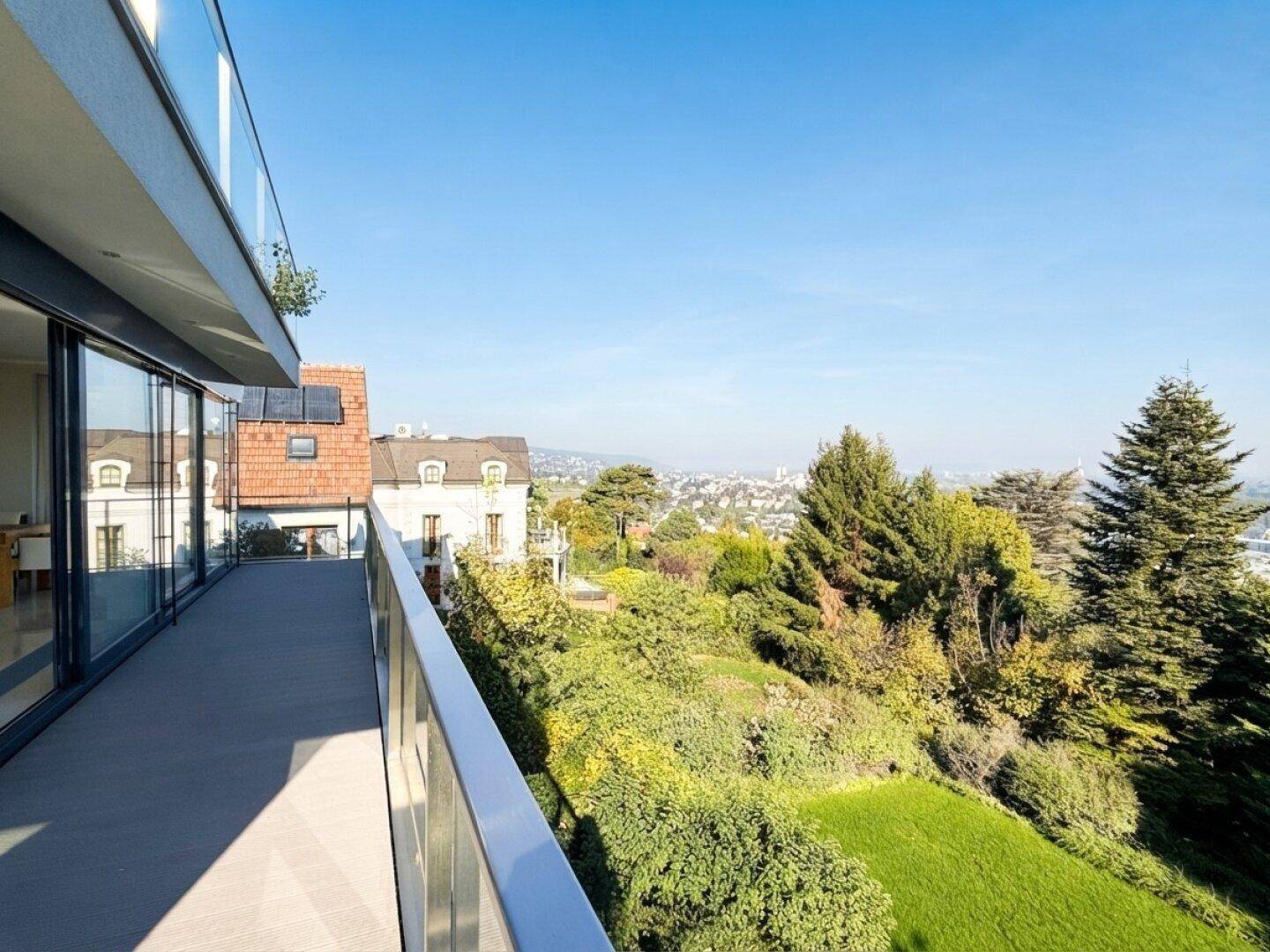Langer Balkon mit Glasgeländer und weitem Blick über die Stadt und die umliegende Natur.