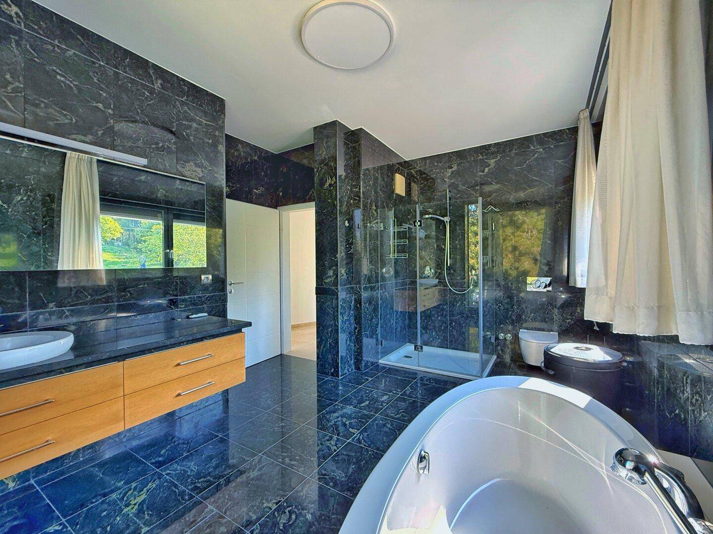 Elegantes Badezimmer mit begehbarer Dusche, Doppelwaschbecken und dunklen Marmoroberflächen.