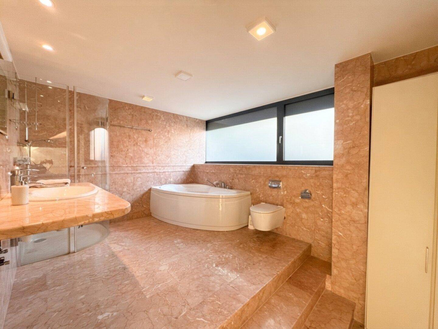 Luxuriöses Badezimmer mit rosafarbenen Marmorfliesen, Whirlpool-Badewanne und großer Dusche.