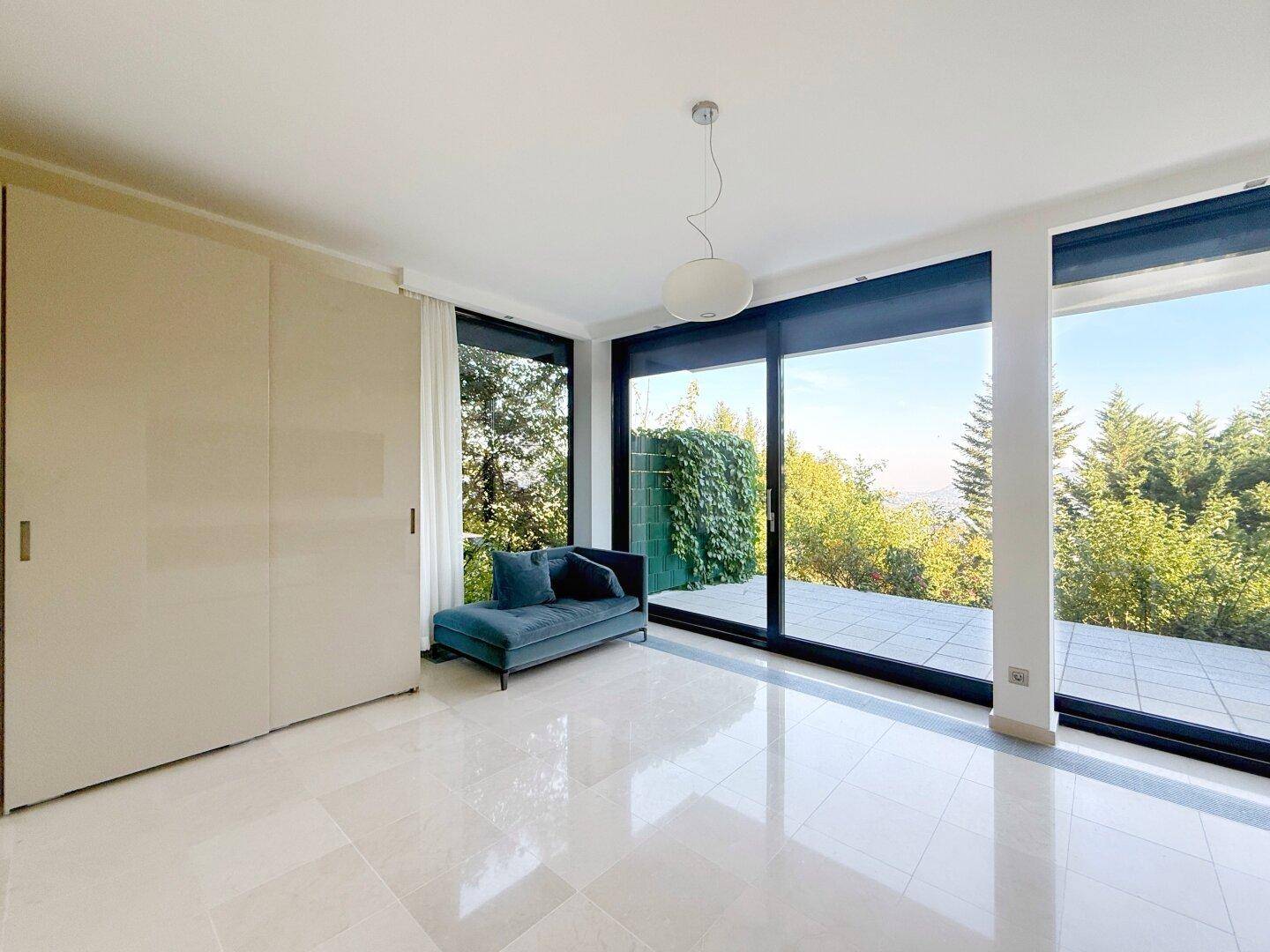 Helles Schlafzimmer mit großen Fensterfronten, Zugang zur Terrasse und integriertem Kleiderschrank.