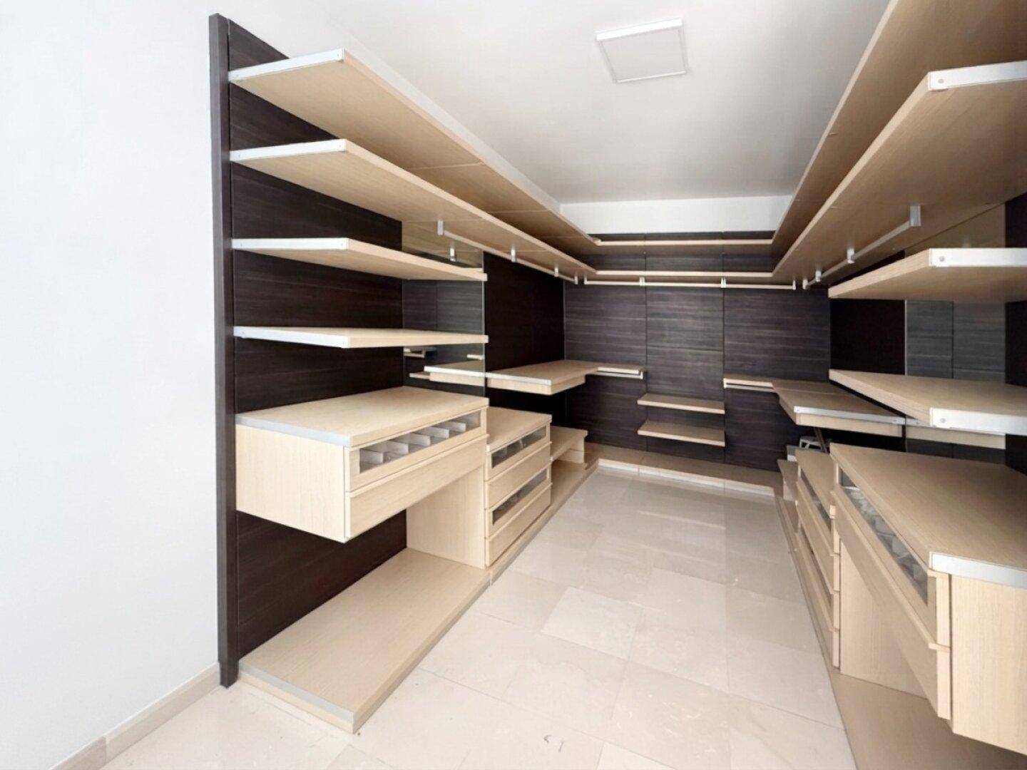 Geräumiger begehbarer Kleiderschrank mit maßgefertigten Regalen und Schubladen in Holzoptik.
