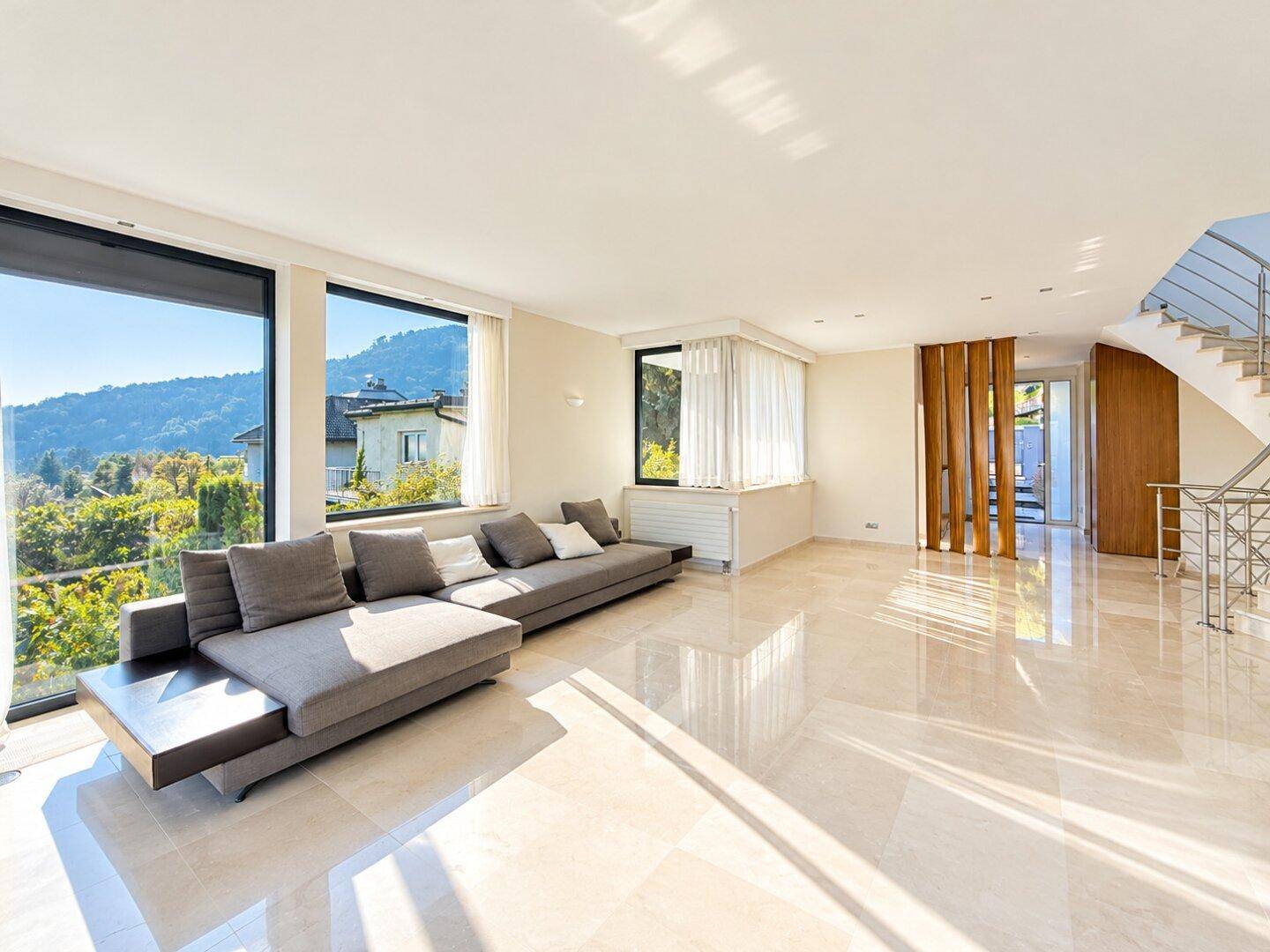 Großzügiges Wohnzimmer mit bequemer Couch, Marmorboden und raumhohen Fenstern mit Weitblick.