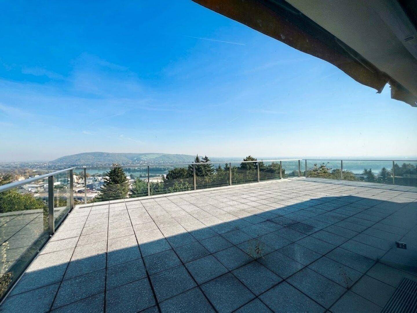Große geflieste Terrasse mit Glasgeländer und weitem Blick über die Landschaft und den See.