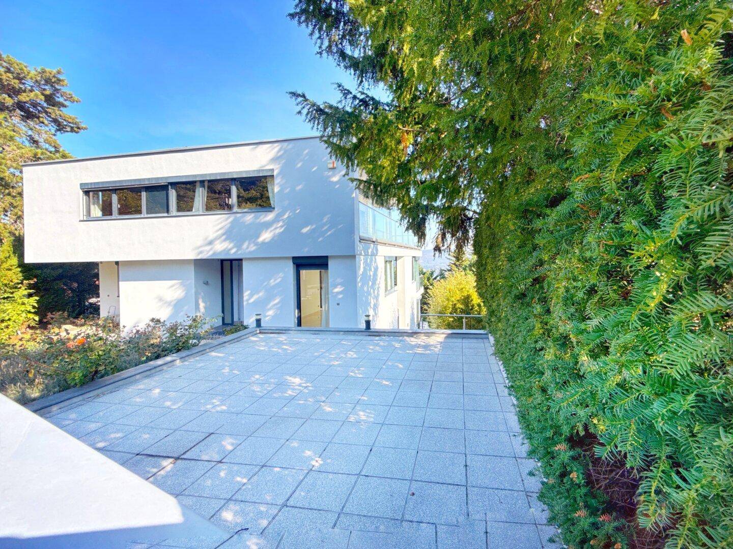 Moderne weiße Villa mit großer gepflasterter Auffahrt und hohen Hecken für Privatsphäre.