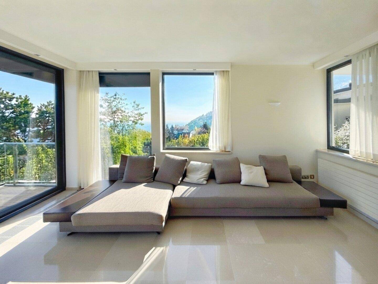 Helles Wohnzimmer mit moderner Couch und großen Fenstern, die einen Panoramablick auf die Umgebung ermöglichen.