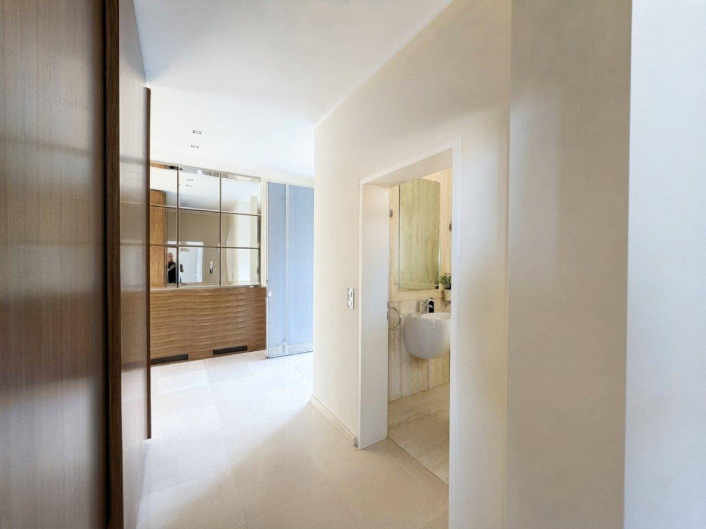 Heller Flur mit modernen Einbauschränken und Zugang zu einem Badezimmer mit Waschbecken.