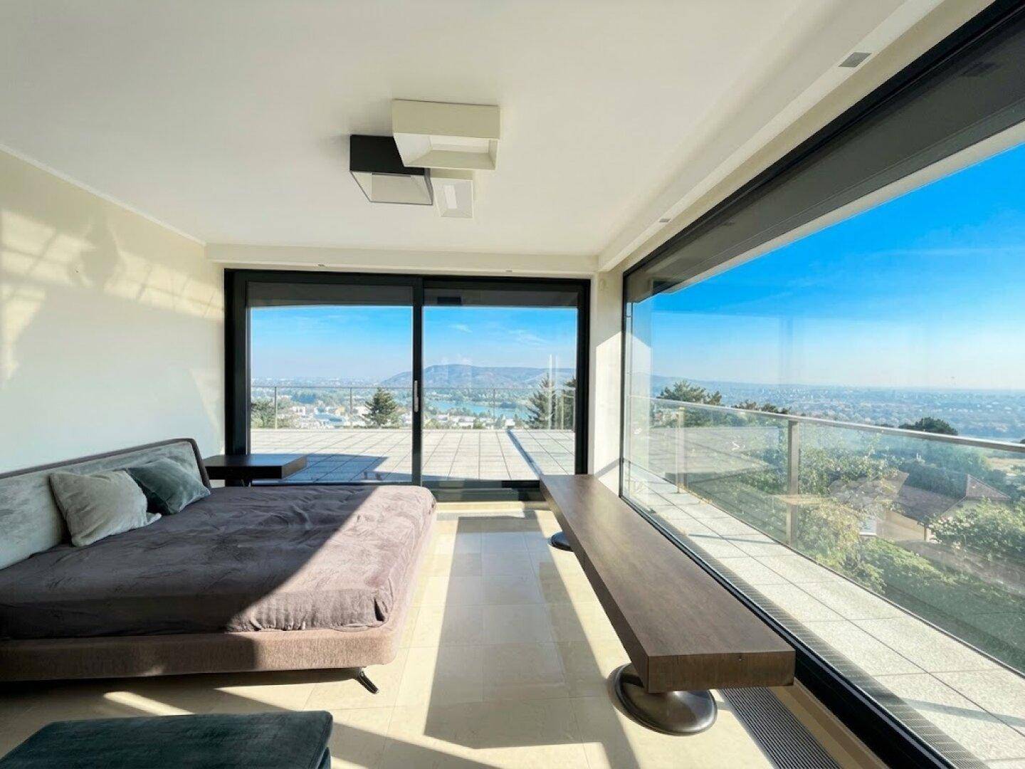 Modernes Schlafzimmer mit großem Bett und raumhohen Fenstern, die einen spektakulären Panoramablick bieten.