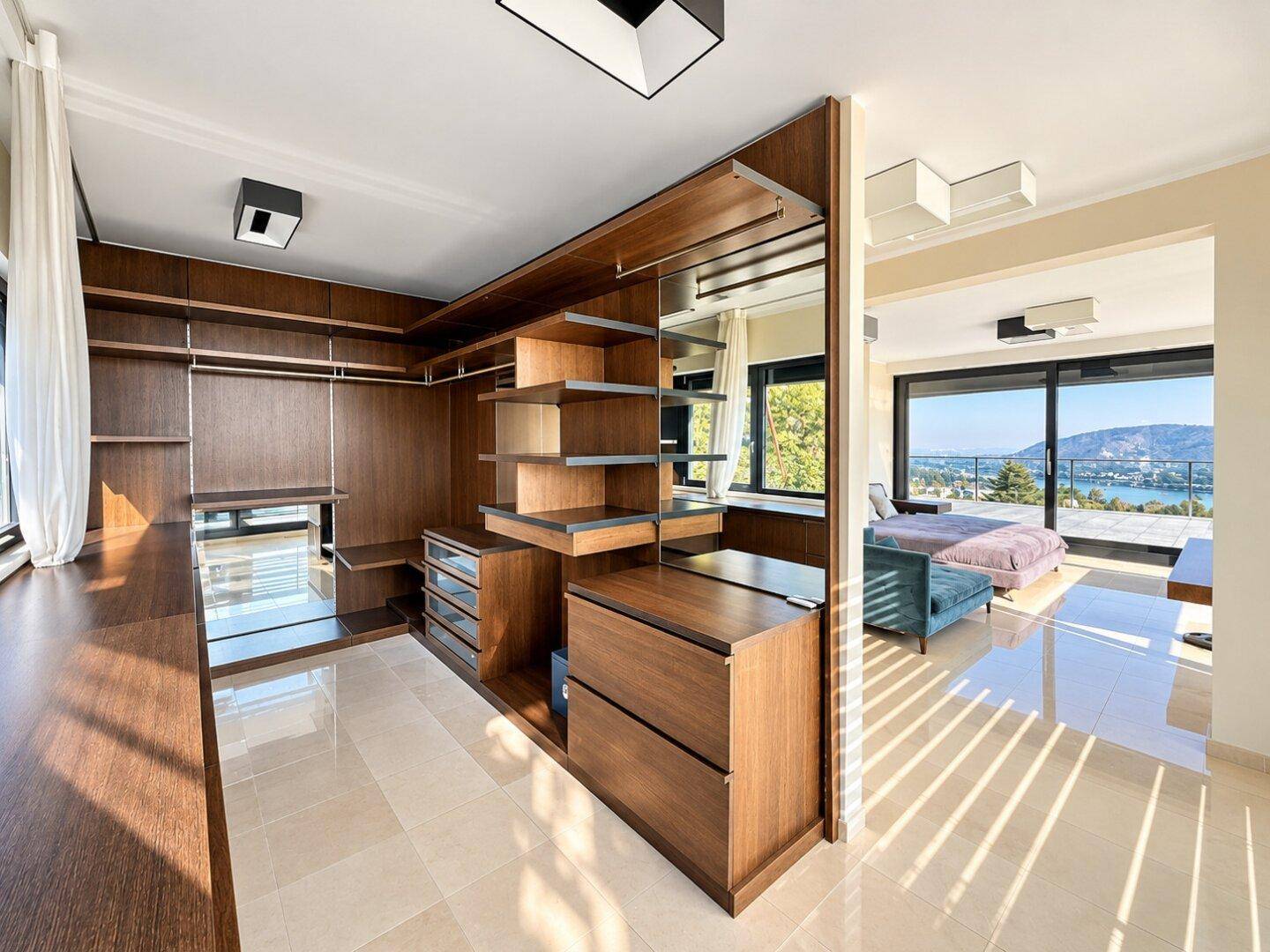 Geräumiger begehbarer Kleiderschrank mit maßgefertigten Holzschränken und Blick ins Schlafzimmer.
