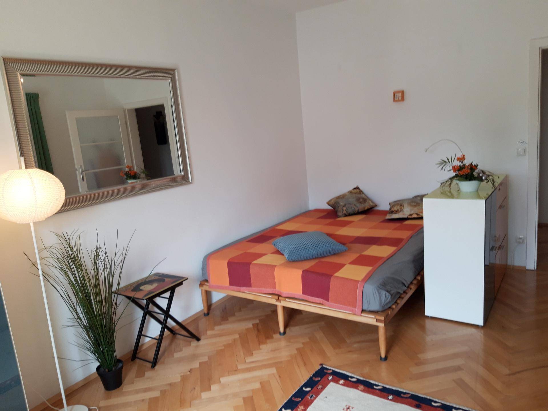 Helles Schlafzimmer mit Holzbett, großem Spiegel und Fischgrätparkettboden.